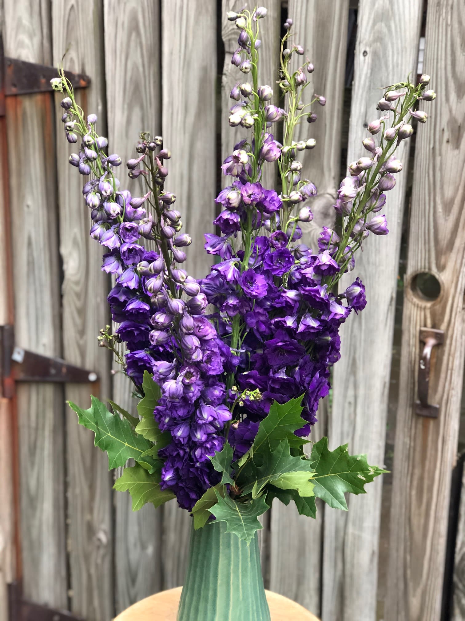 Tall purple flower arrangement in a green vase with leafy accents