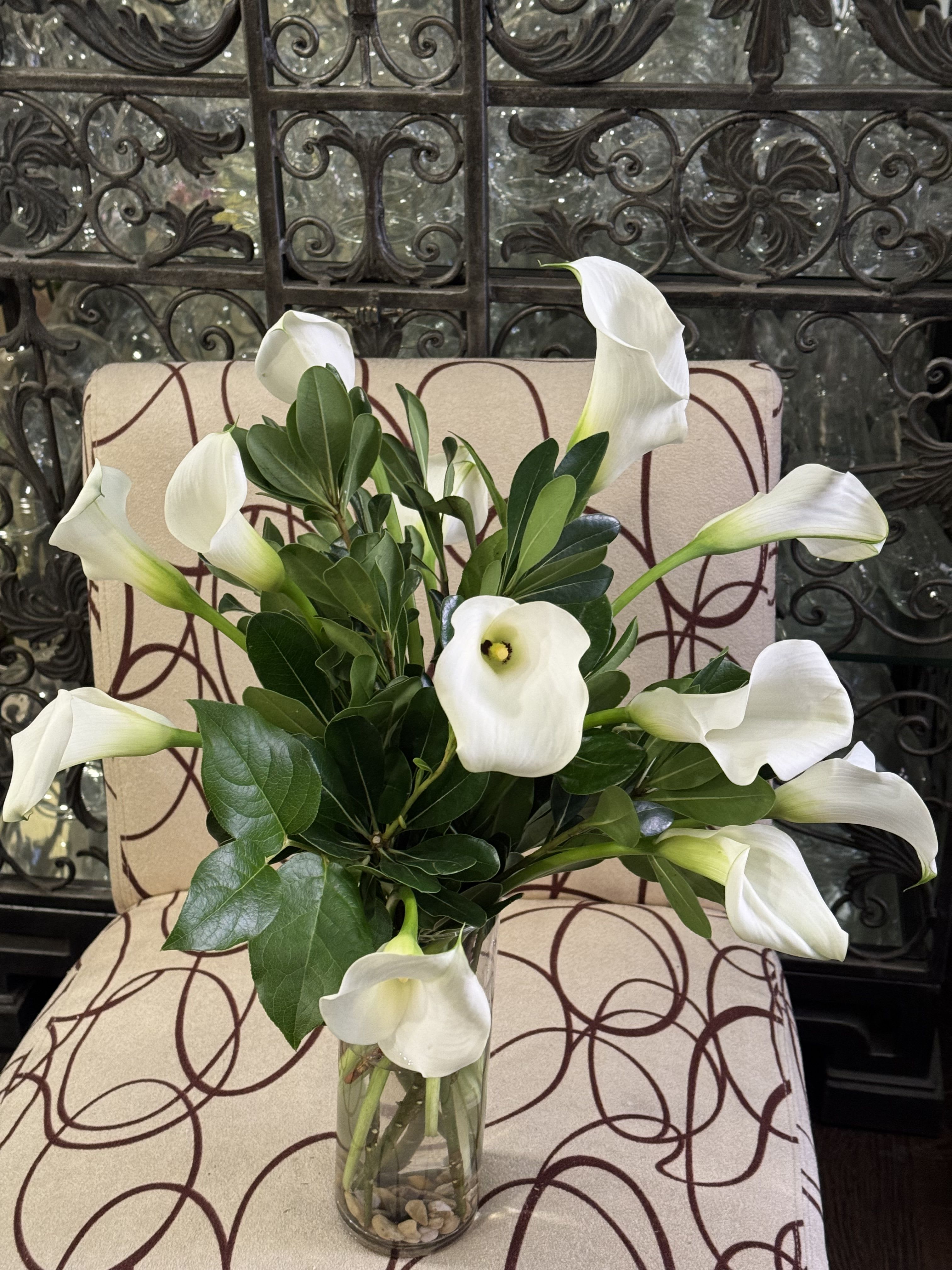 White calla lilies arranged in a clear glass vase with glossy green foliage.