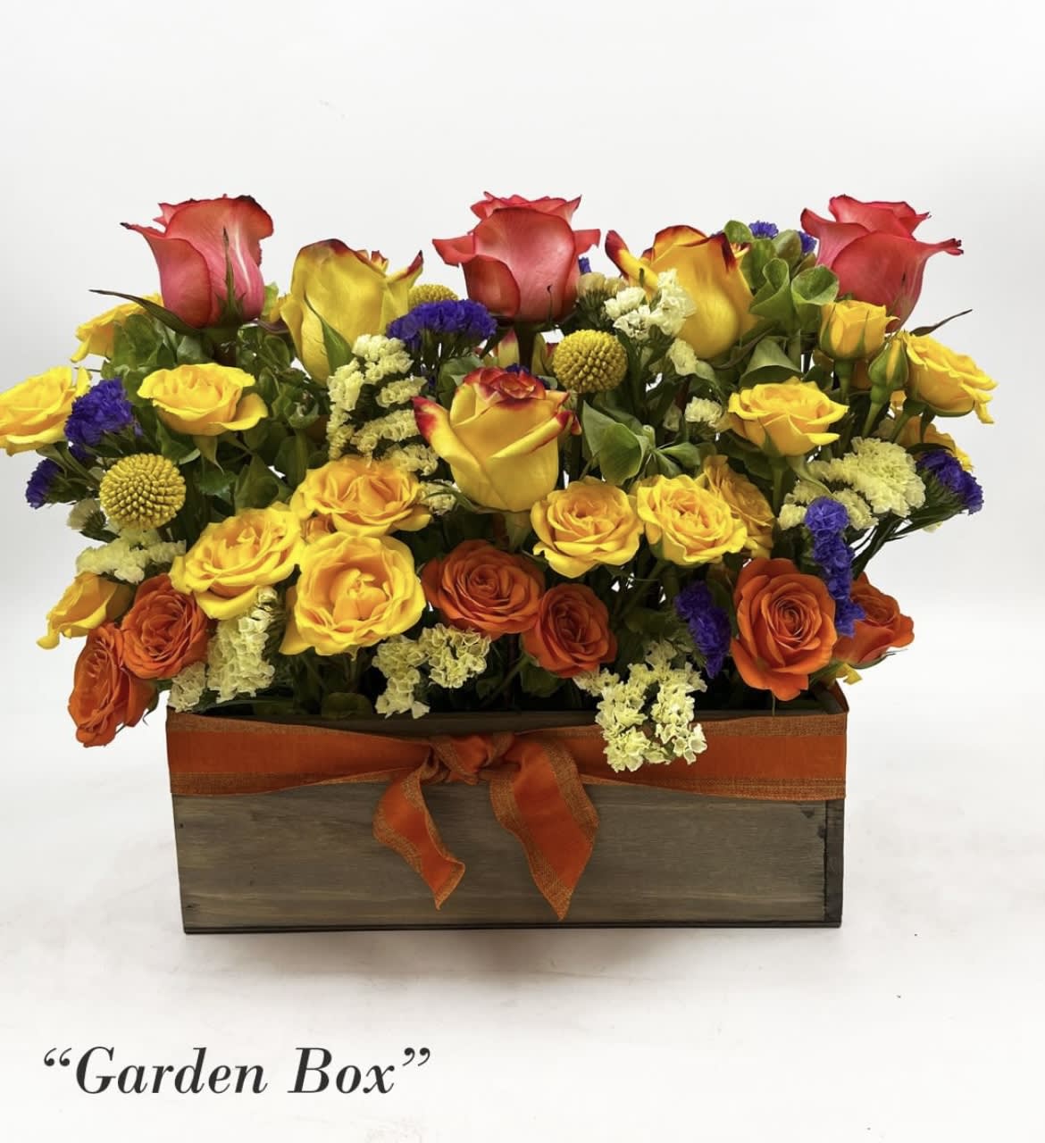Mixed roses and small filler flowers arranged in a wooden box with an orange ribbon.