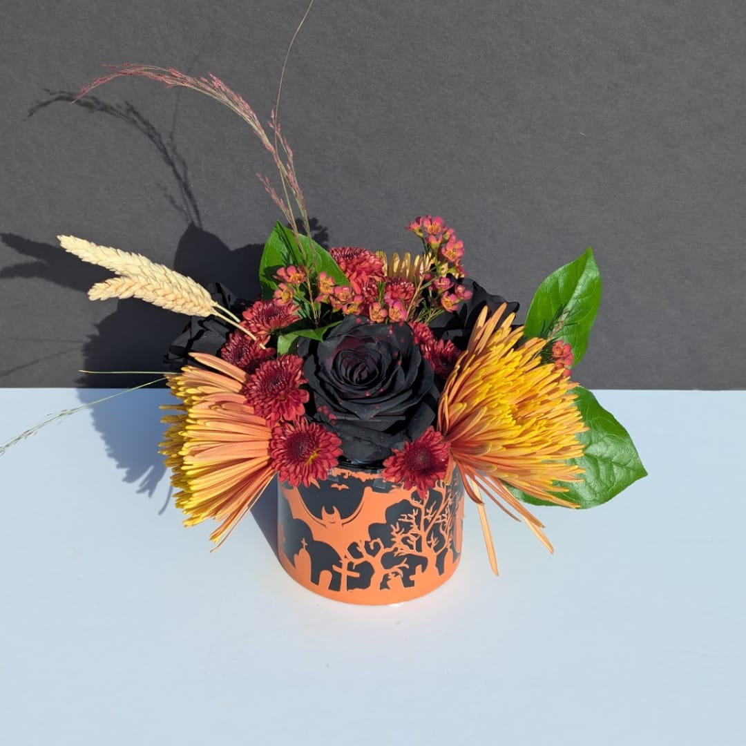 Halloween floral arrangement in an orange-and-black container with a black rose