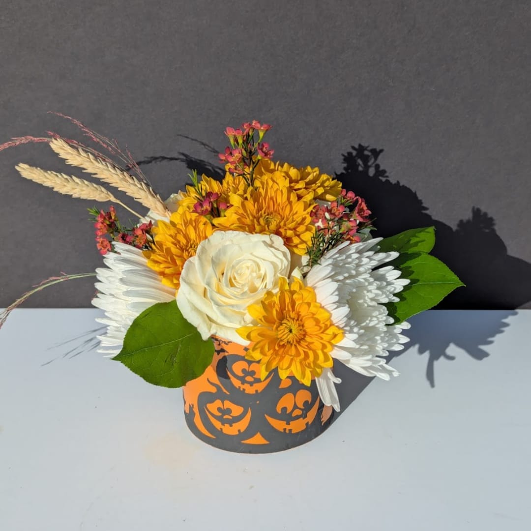 Yellow and white floral arrangement in a Halloween pumpkin container