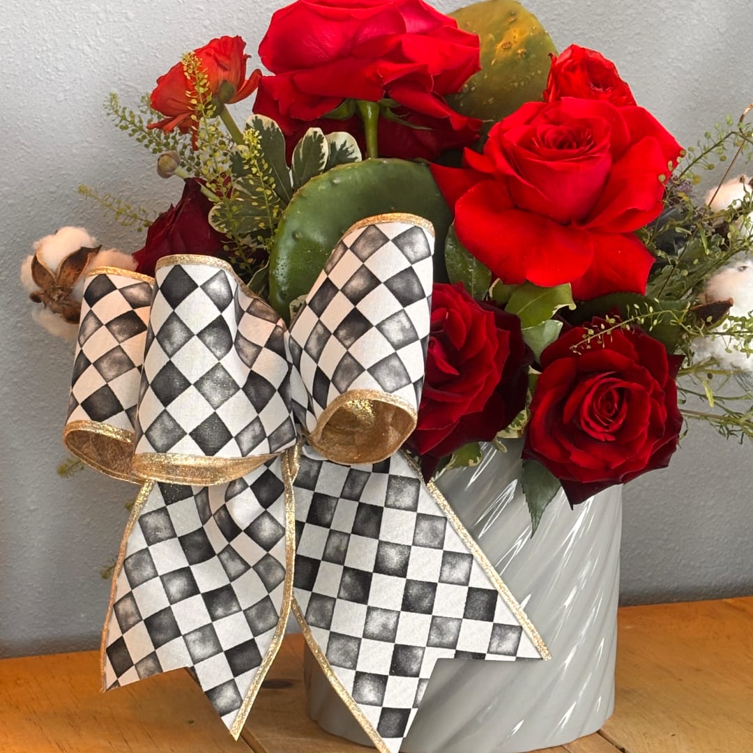 Red roses arranged in a white vase with a black-and-white checkered bow