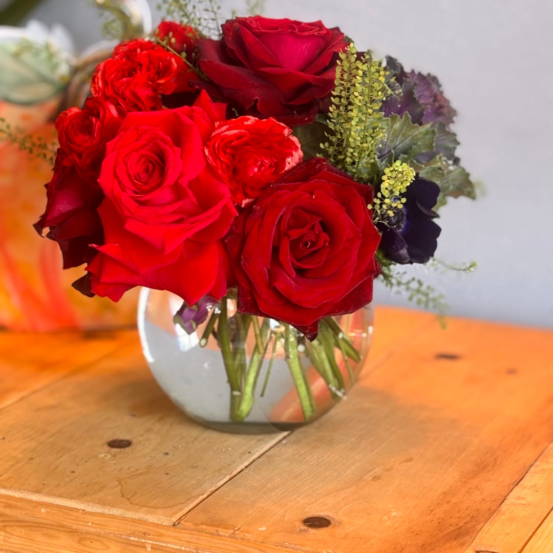 Red rose bouquet in a clear glass vase on a wooden table