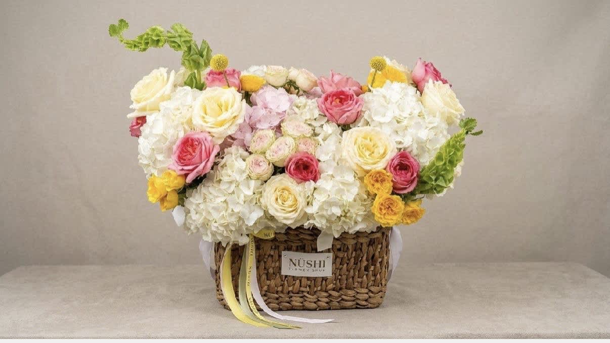 Basket arrangement of white and pink roses with yellow accents