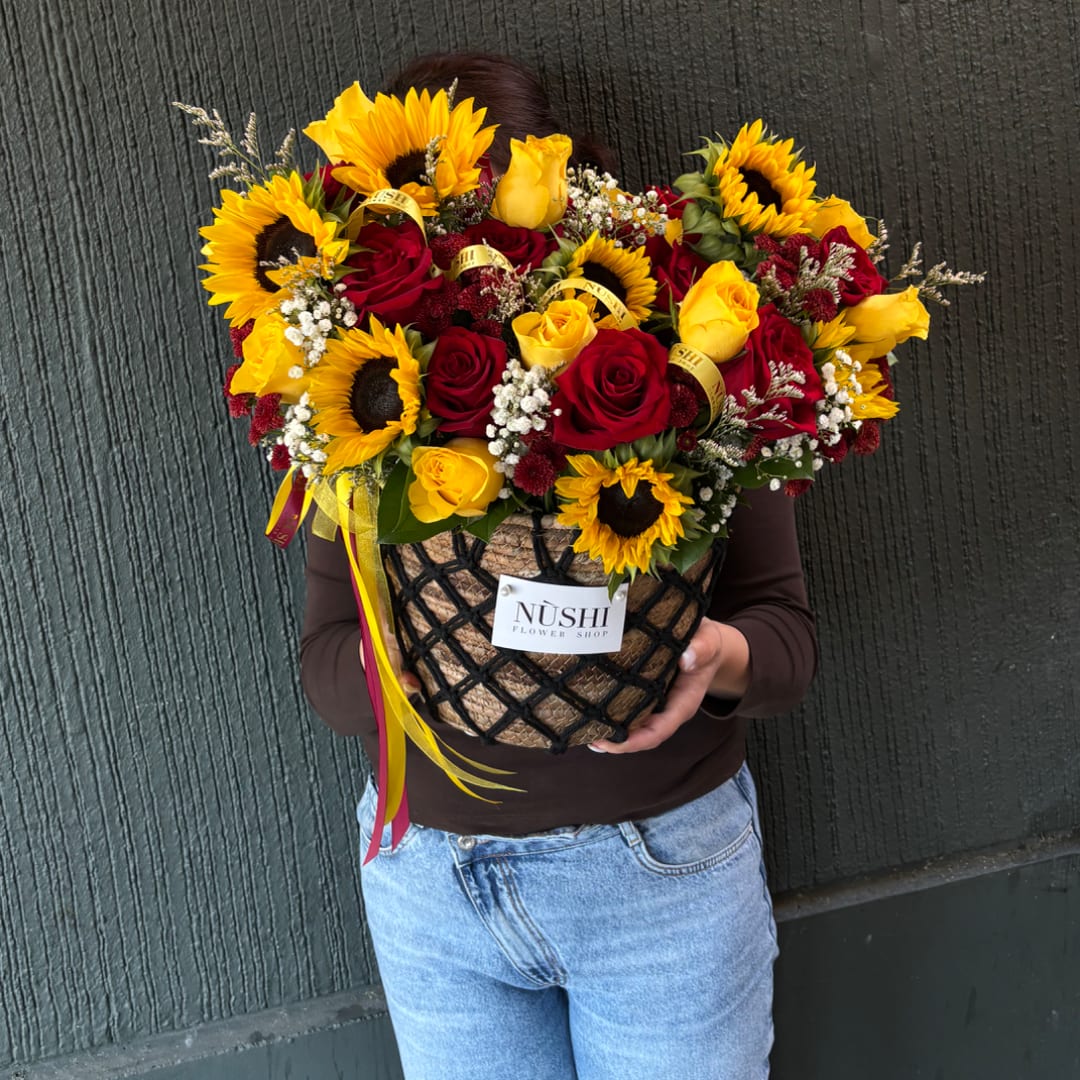 Large bouquet of red and yellow roses with sunflowers in a woven basket