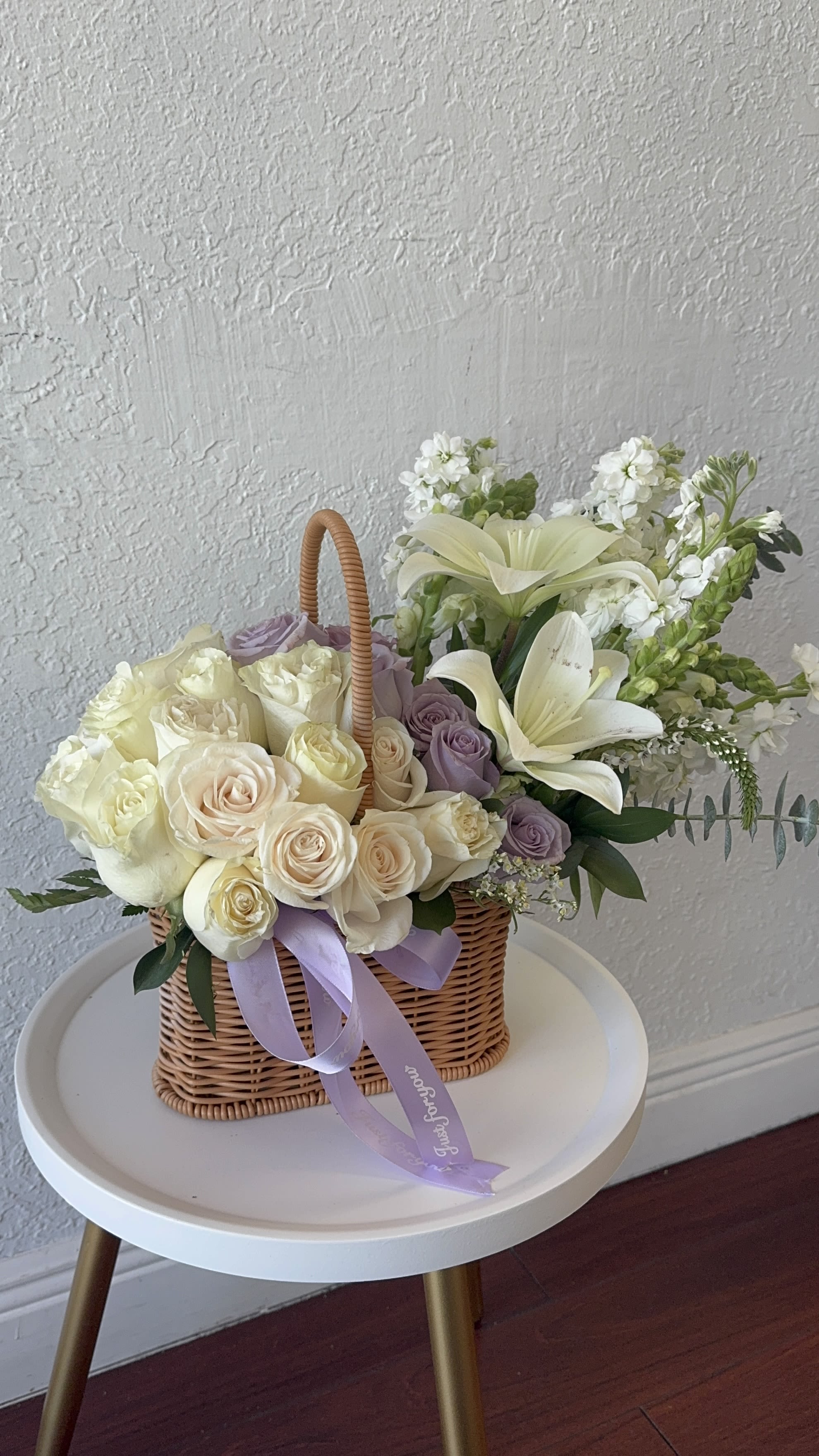 Basket of cream and lavender roses with white lilies and ribbon