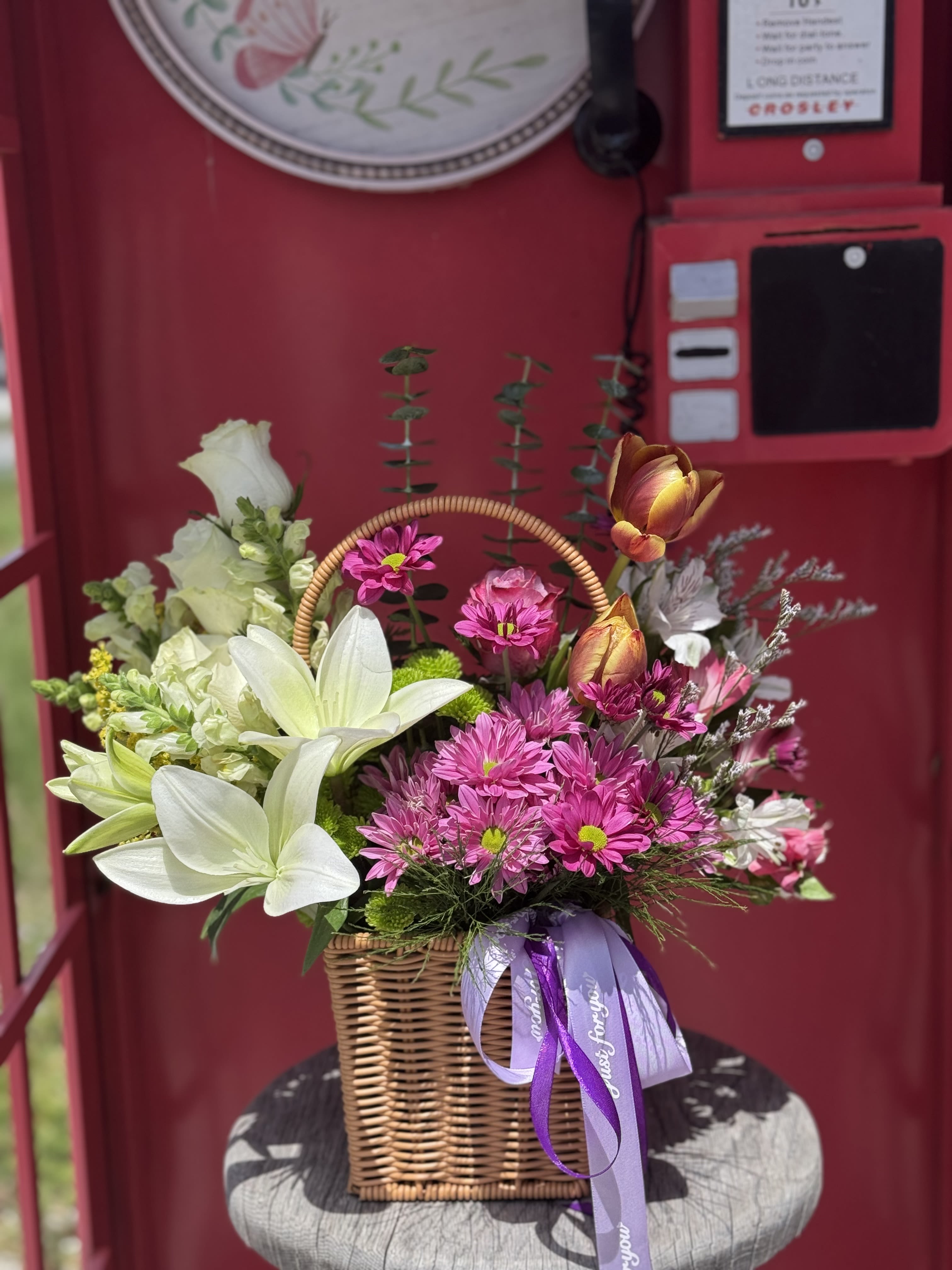 Basket arrangement of white lilies and pink daisies with a purple ribbon
