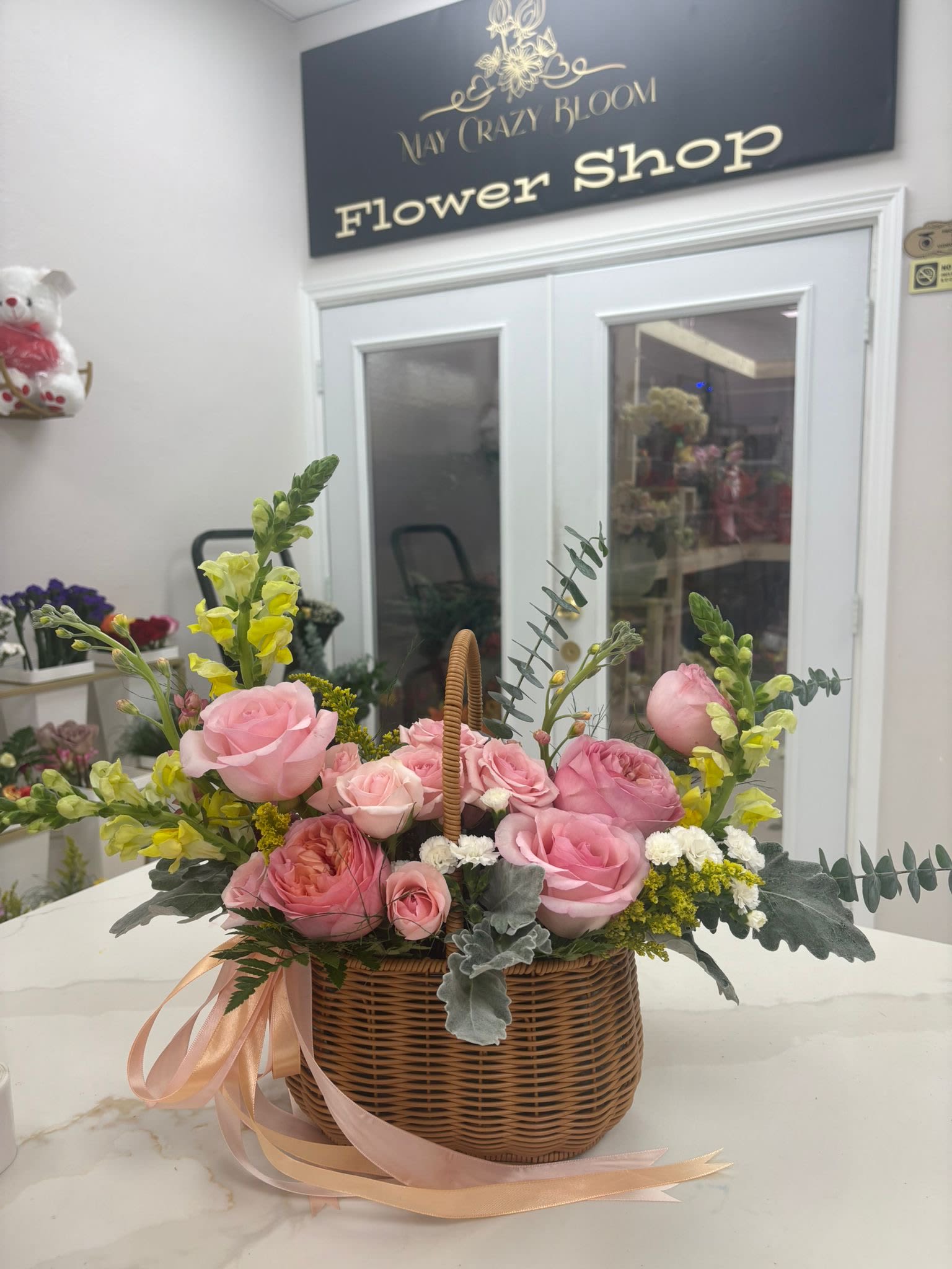 Pink roses and yellow snapdragons in a wicker basket with ribbon