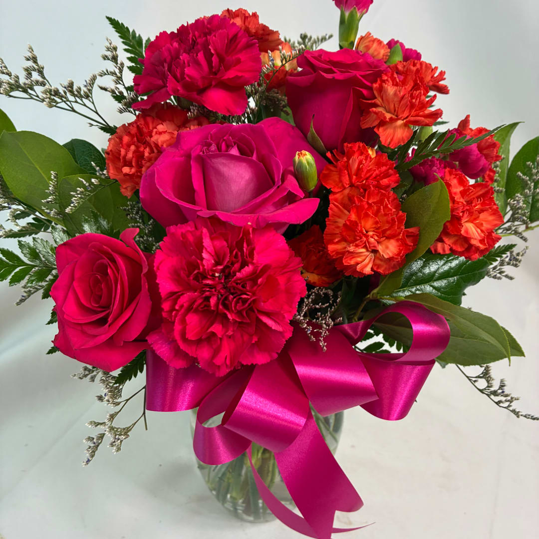 Pink roses and orange carnations in a glass vase with a magenta ribbon
