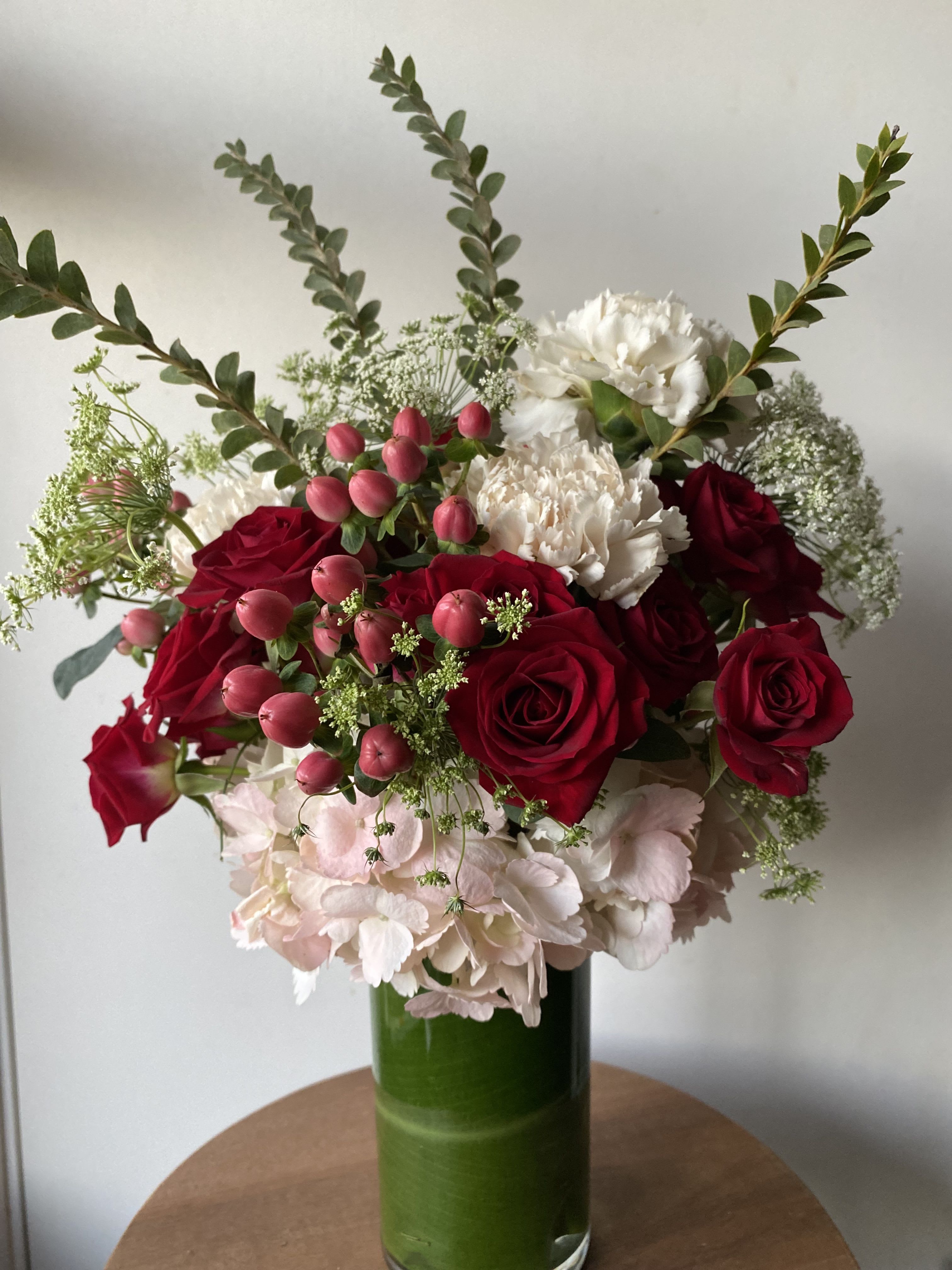 Bouquet of red roses, white carnations, and pink berries in a green glass vase