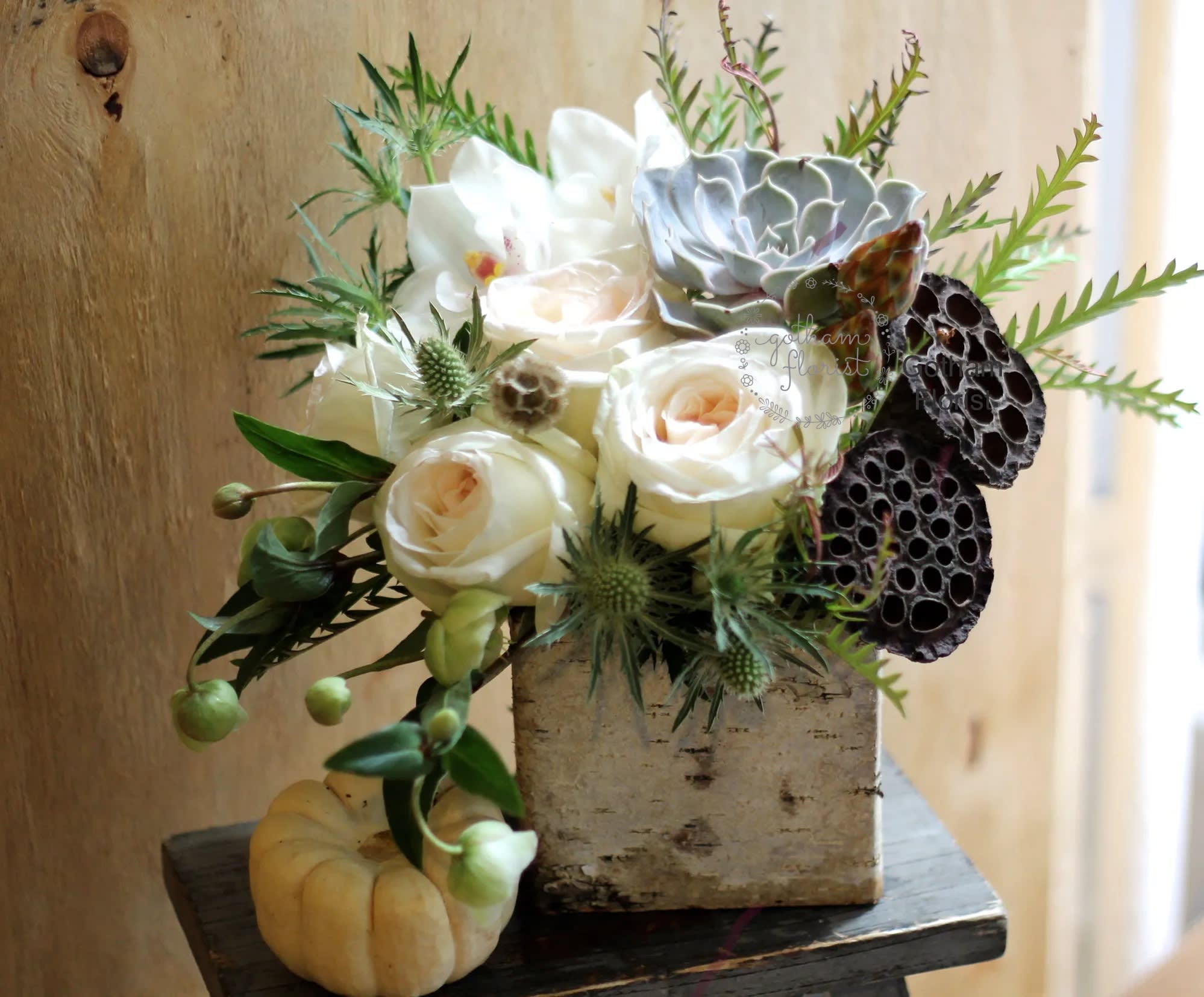 White roses and succulents in a rustic square container with lotus pods