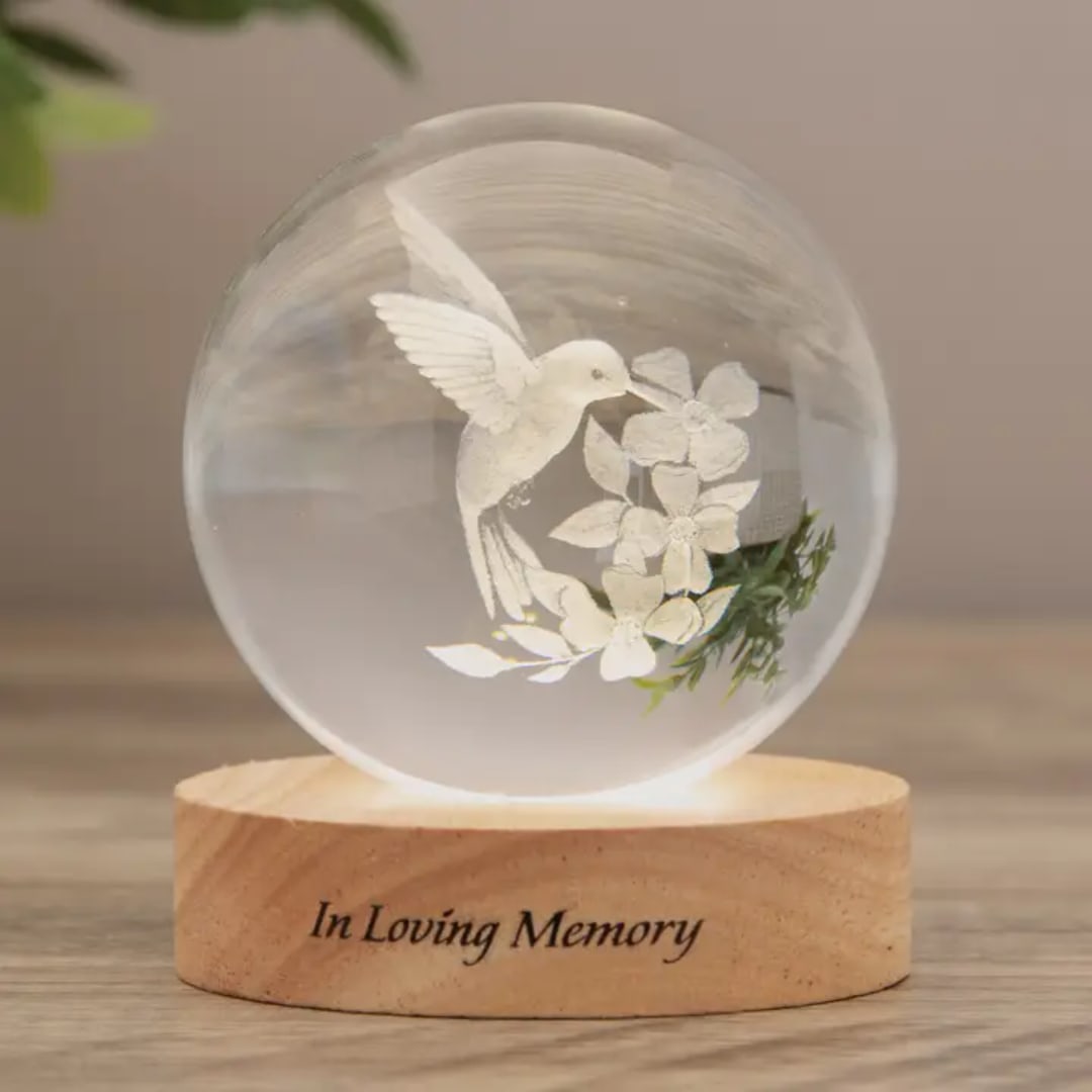 Glass orb memorial light with a white hummingbird and flowers on a wooden base