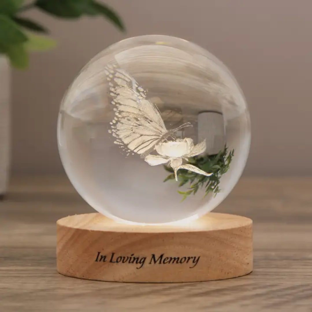 Butterfly and flower inside a clear glass orb on a wooden base