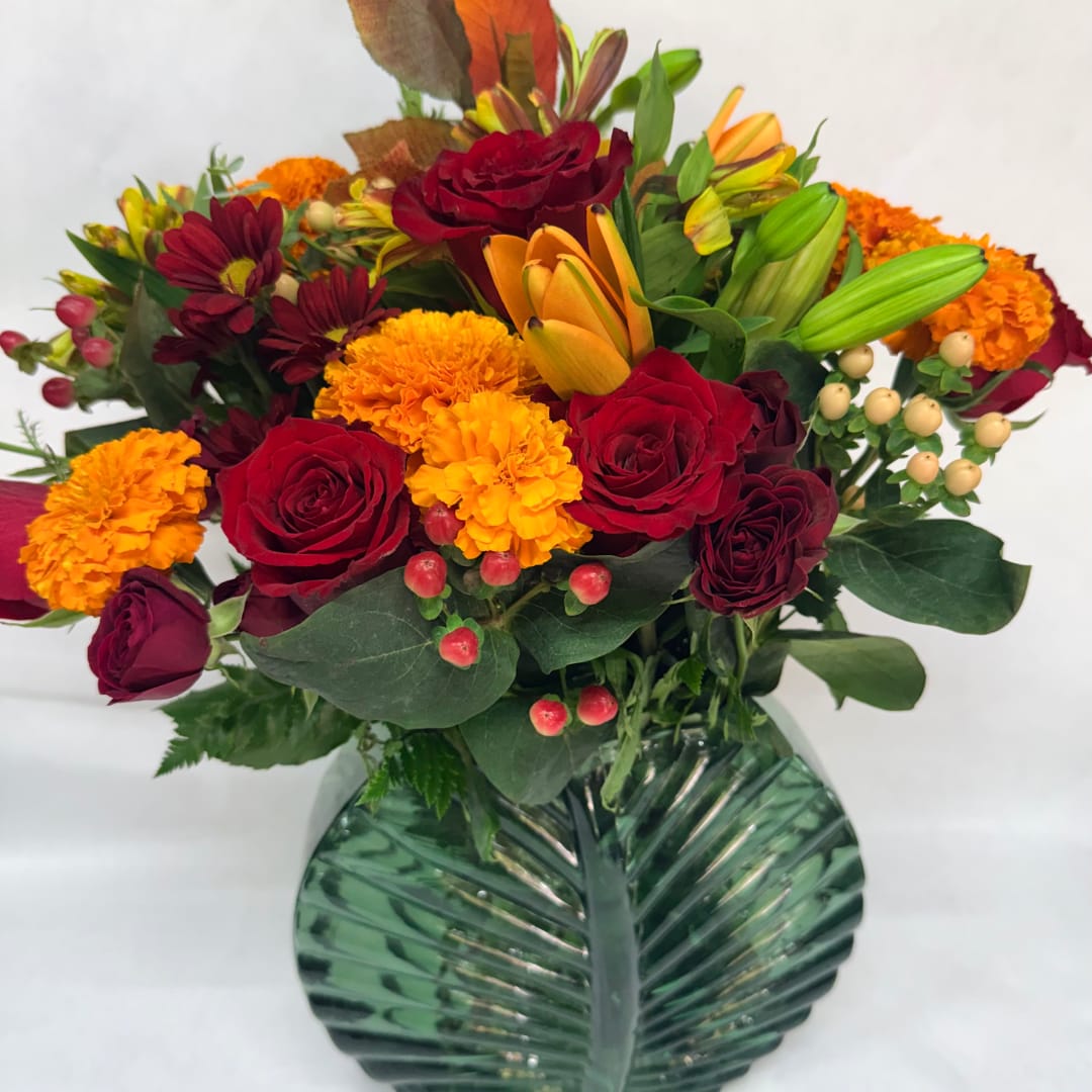 Bouquet of red roses, orange lilies, and marigolds in a green glass vase