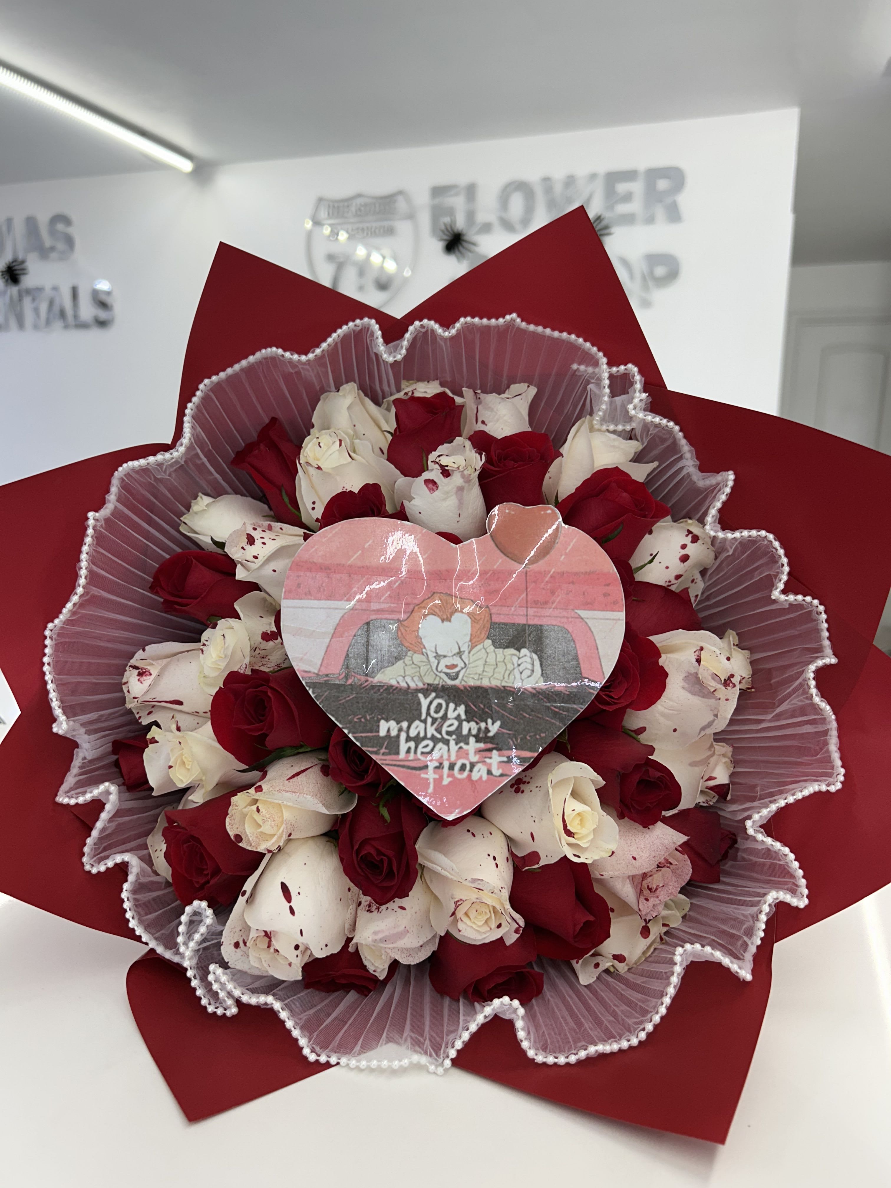 Red and white rose bouquet wrapped in red paper with a heart topper