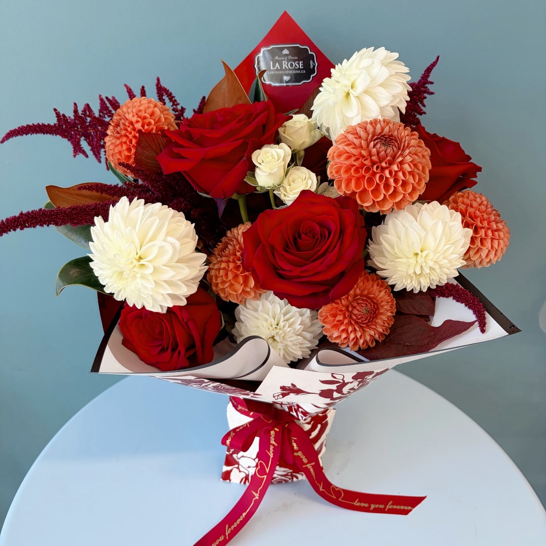 Bouquet of red roses, white dahlias, and peach blooms wrapped in patterned paper
