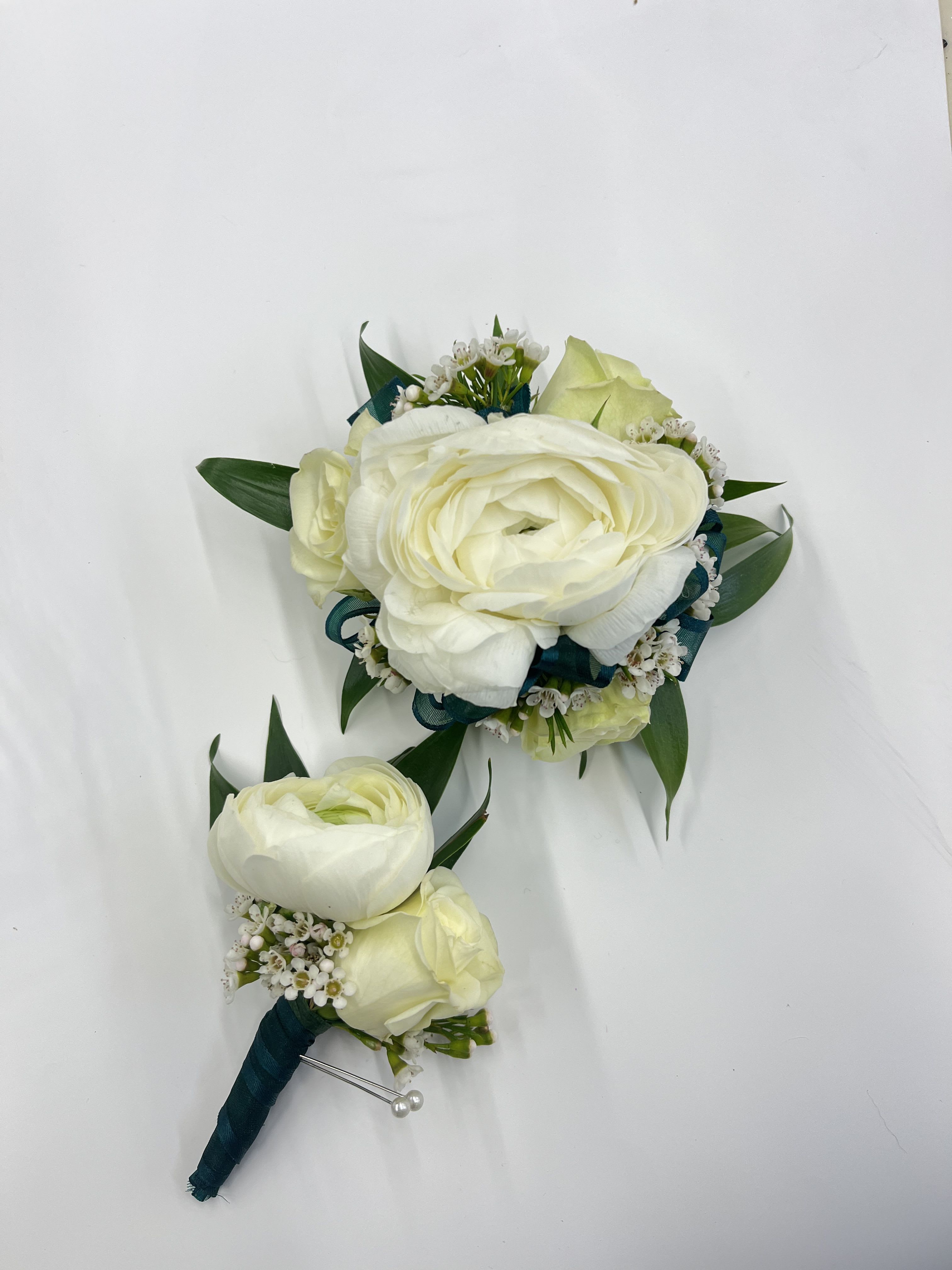 Ranuncula &amp; Rose Corsage/Boutonnière - A white boutonniere and corsage set featuring elegant white roses and ranunculus, accented with soft greenery. The corsage is designed on an adjustable Velcro wristlet for comfort, while the boutonniere is secured with a magnet for easy, pin-free wear. Ribbon color can be customized, please include your preferred color in the special instructions at checkout.
