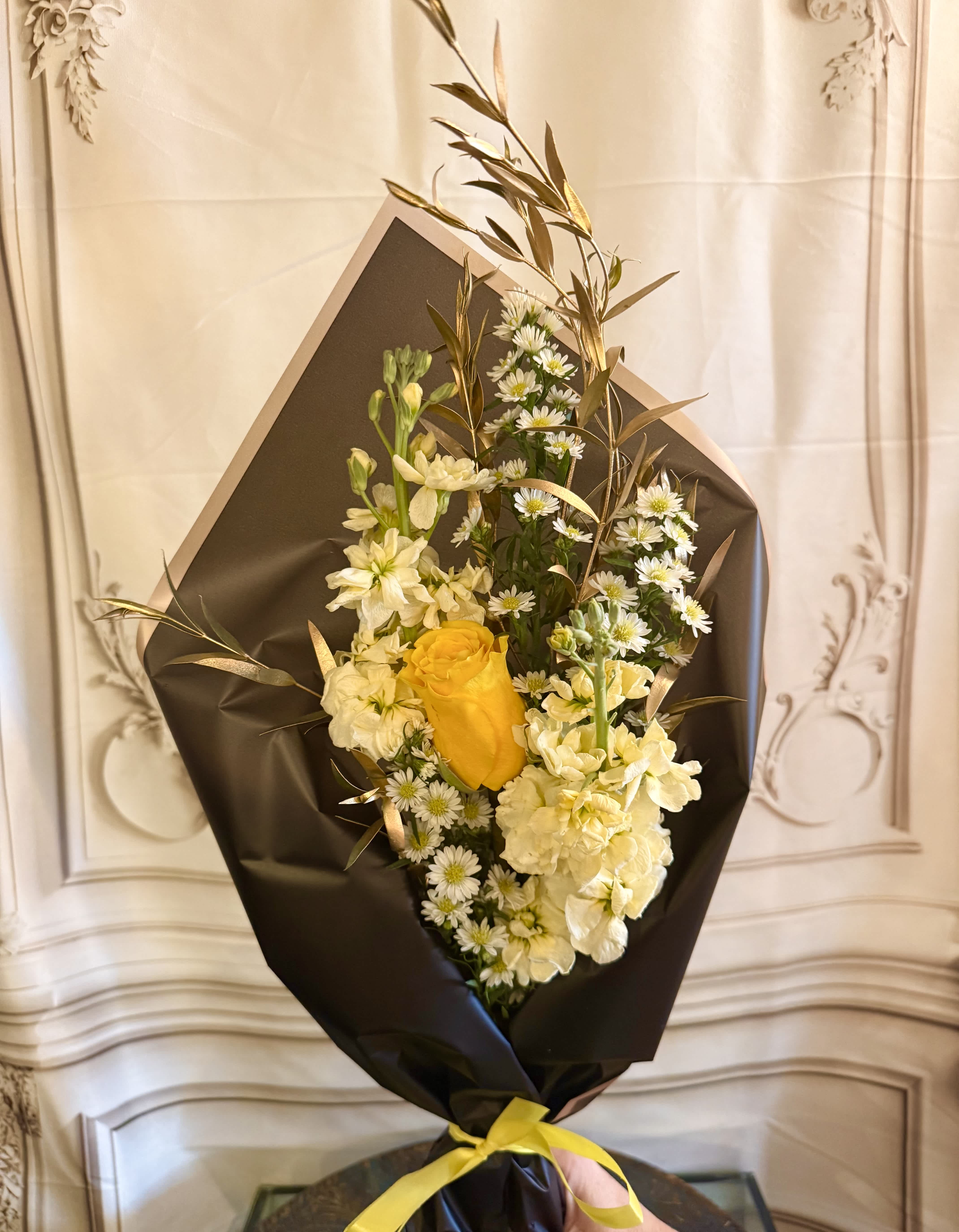 Bouquet of yellow and white flowers wrapped in black paper with a yellow ribbon