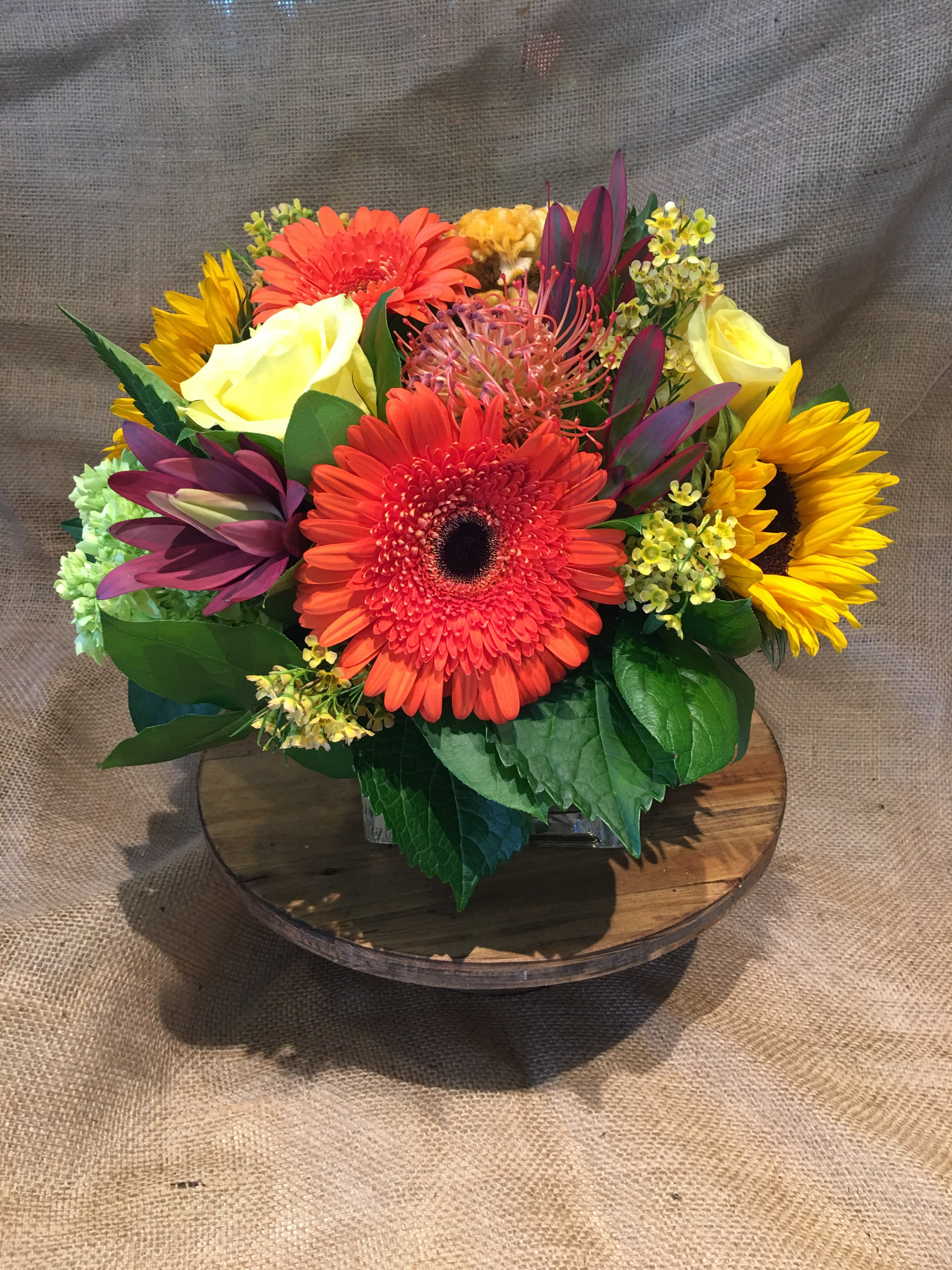 Bright mixed bouquet with gerbera daisies, roses, and sunflowers in a low vase
