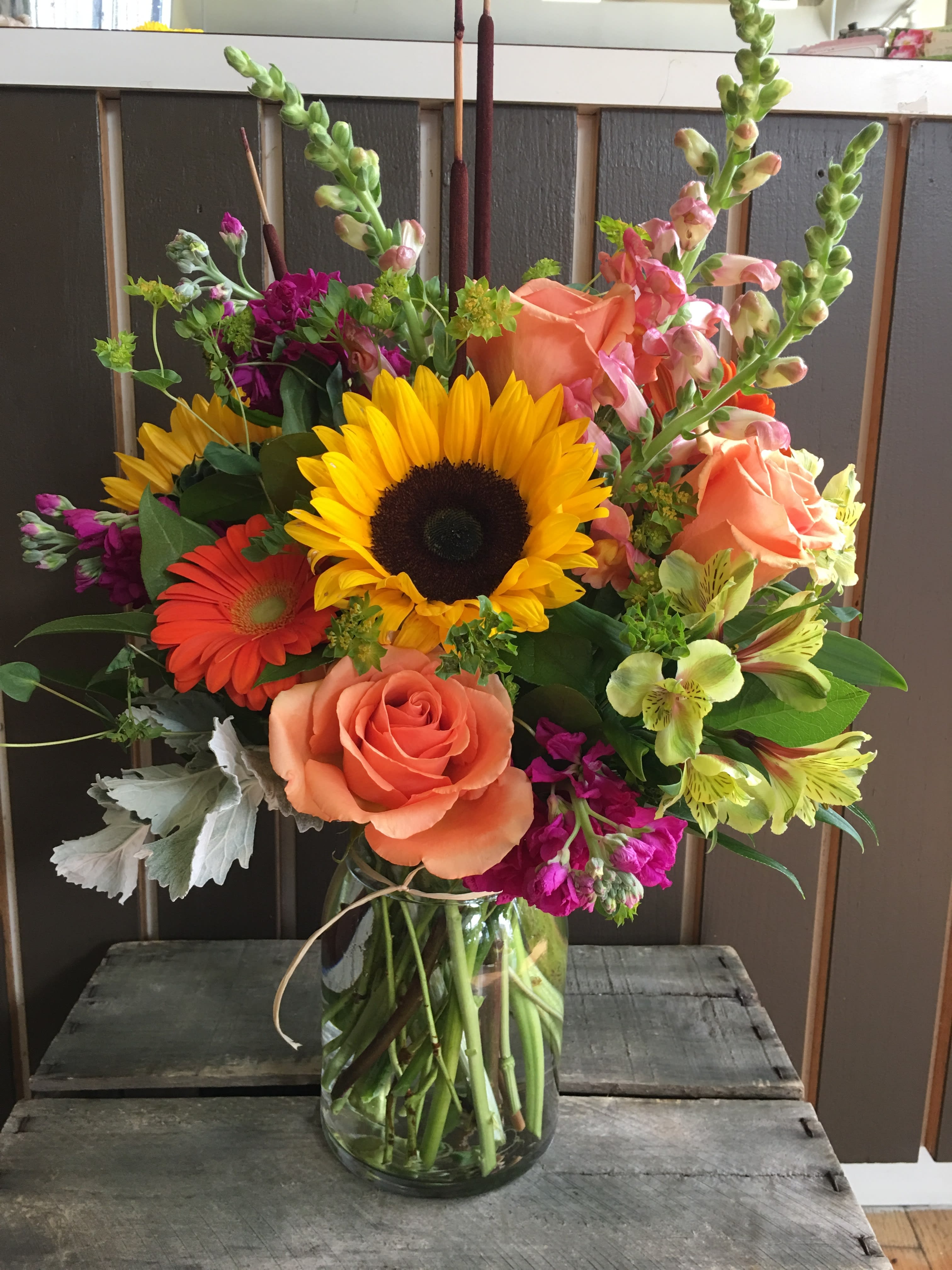 Mixed bouquet with sunflowers, roses, and snapdragons in a glass vase