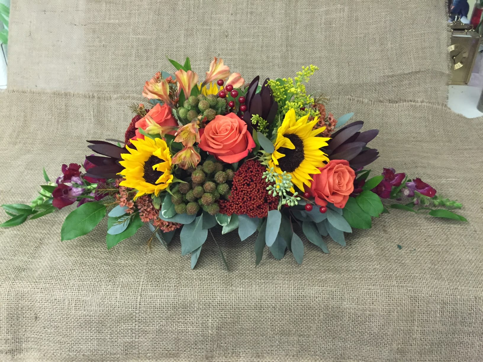 Low floral arrangement with sunflowers and coral roses on a burlap background
