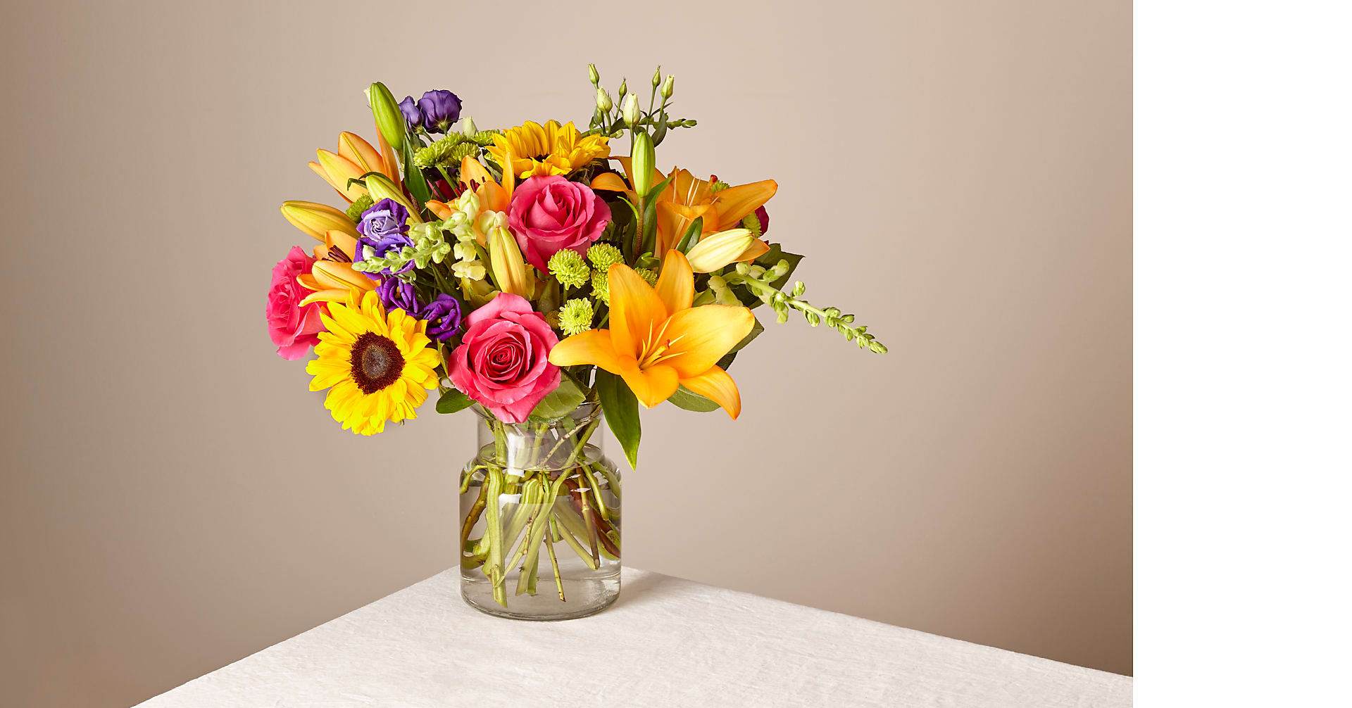 Mixed bouquet of roses, lilies, and sunflowers in a glass vase