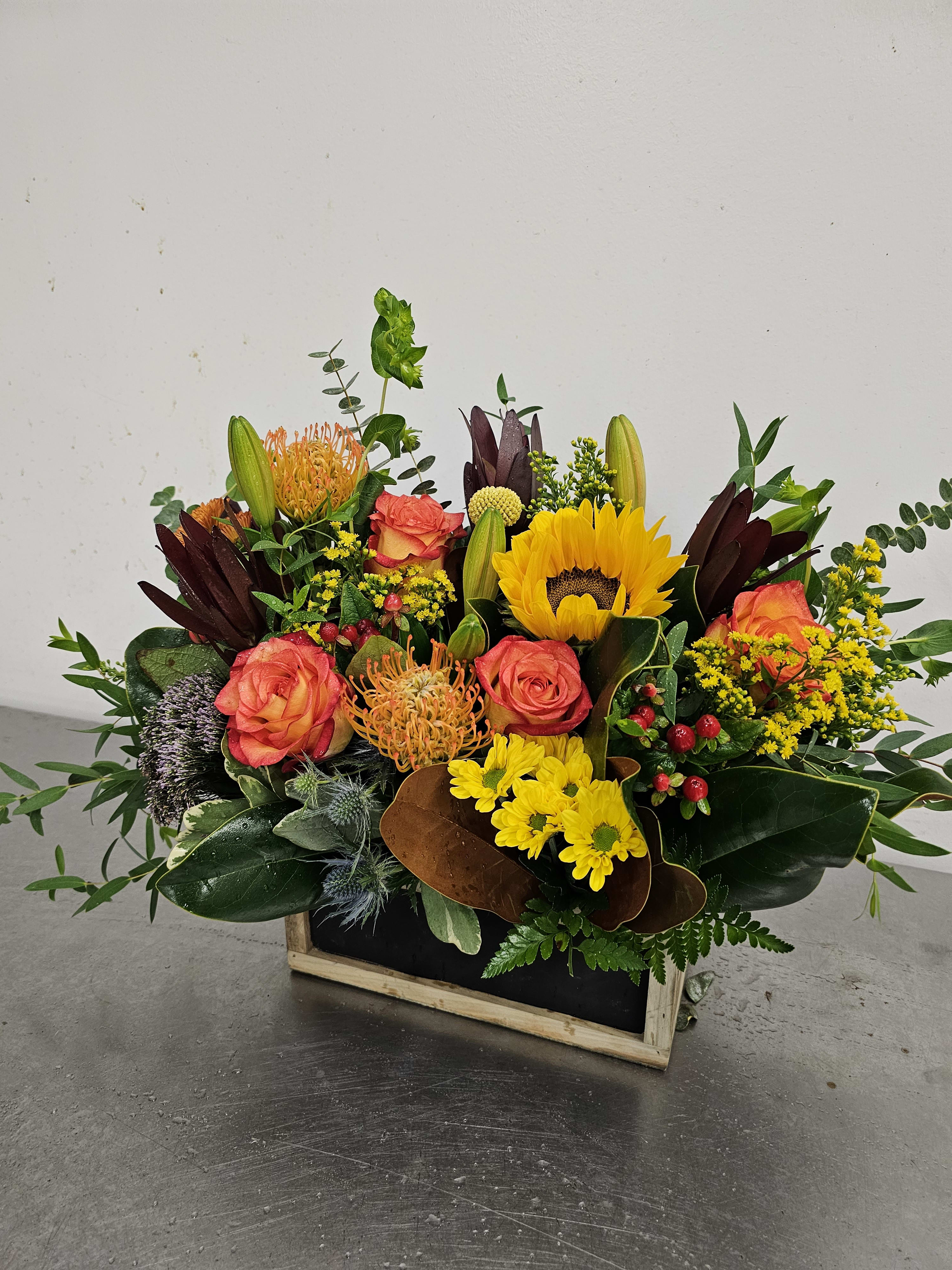 Mixed bouquet with sunflowers, coral roses, and yellow mums in a wooden box