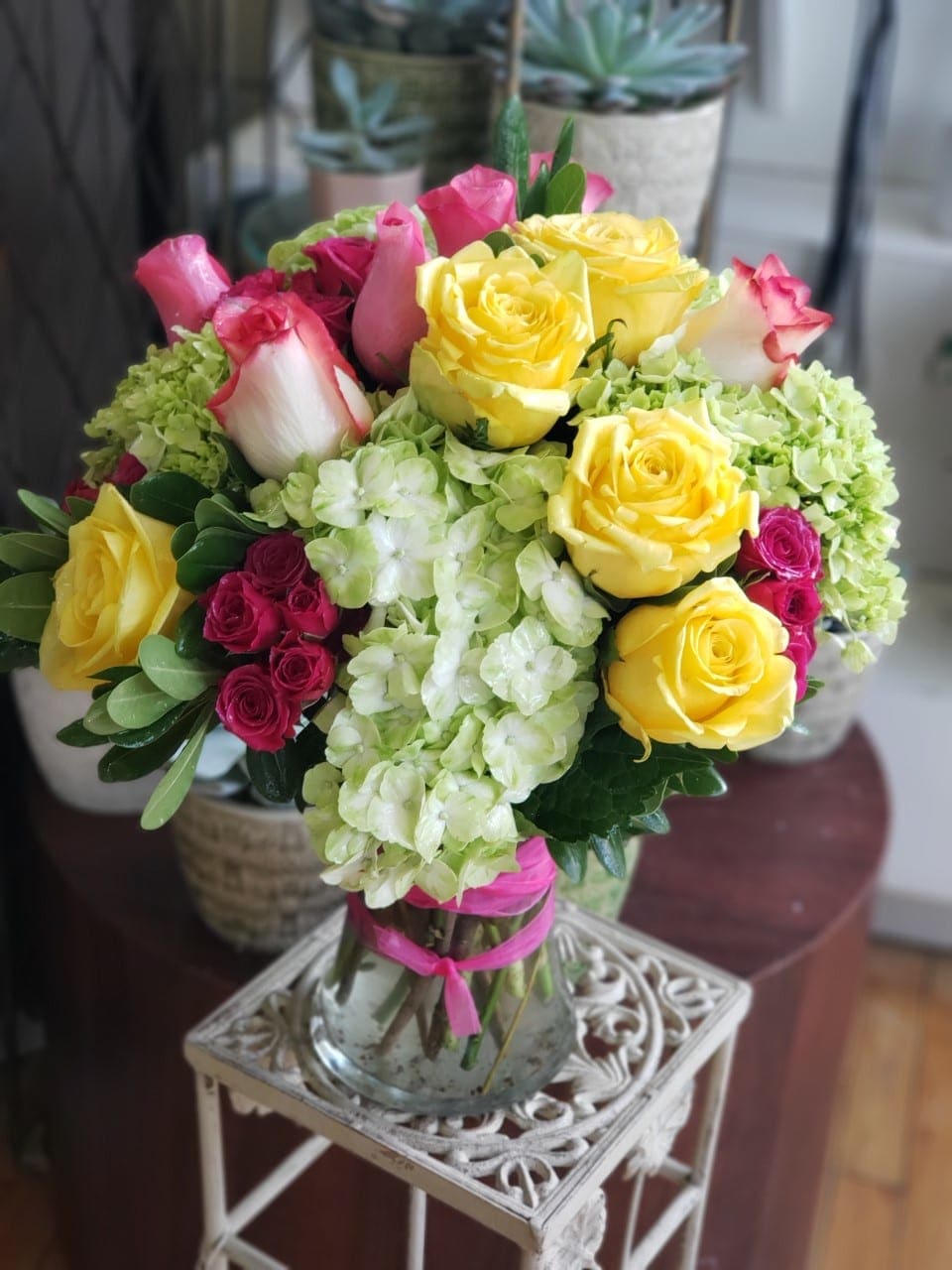 Bouquet of yellow and pink roses with pale green hydrangeas in a glass vase