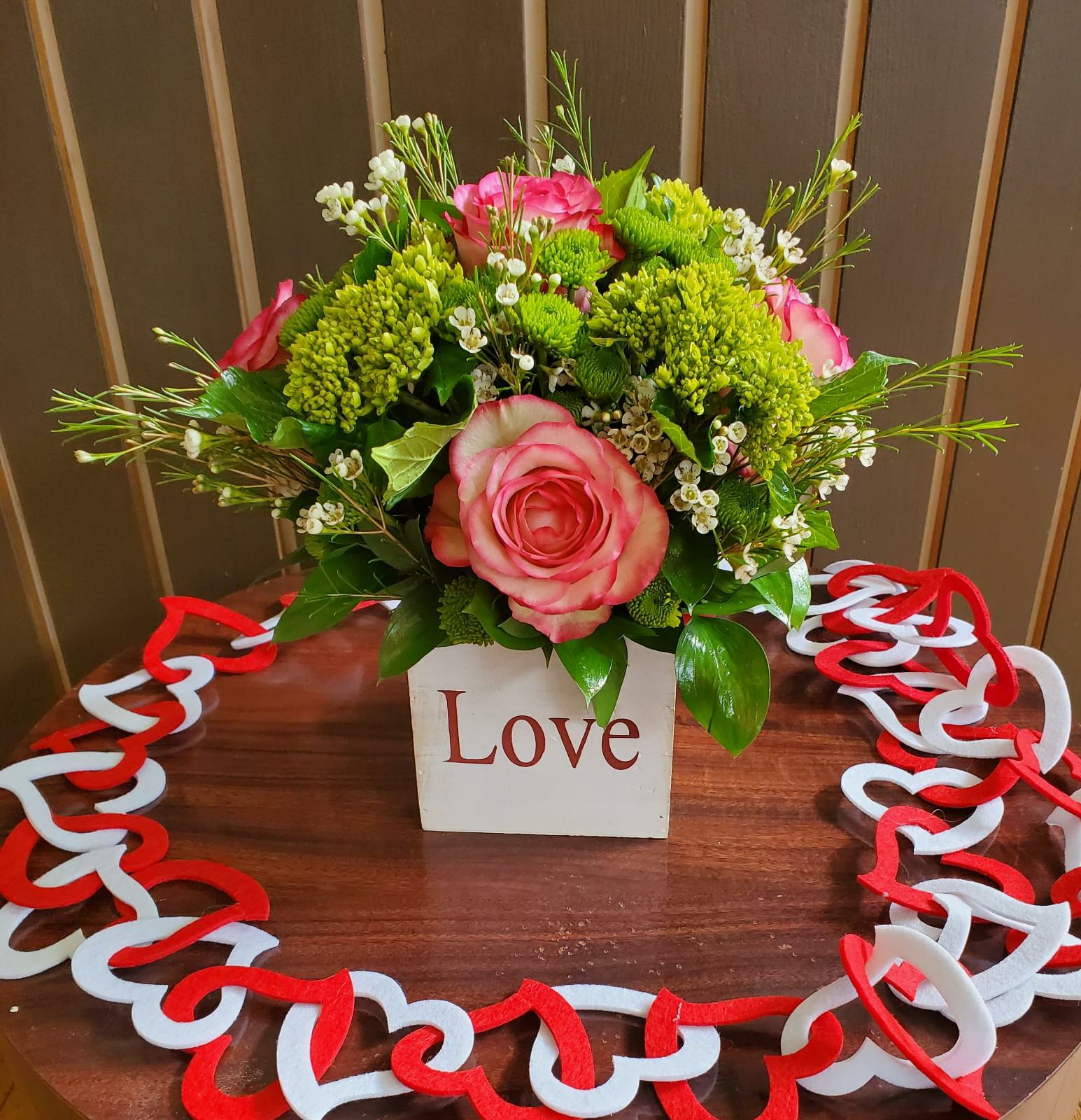 Pink roses and green chrysanthemums in a white box with a heart garland