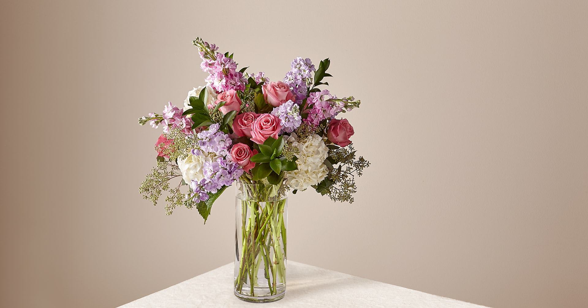 Tall bouquet of pink roses, lavender stock, and white hydrangeas in a clear glass vase