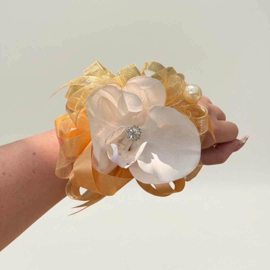 White orchid corsage with gold ribbon and pearl accents on a wrist