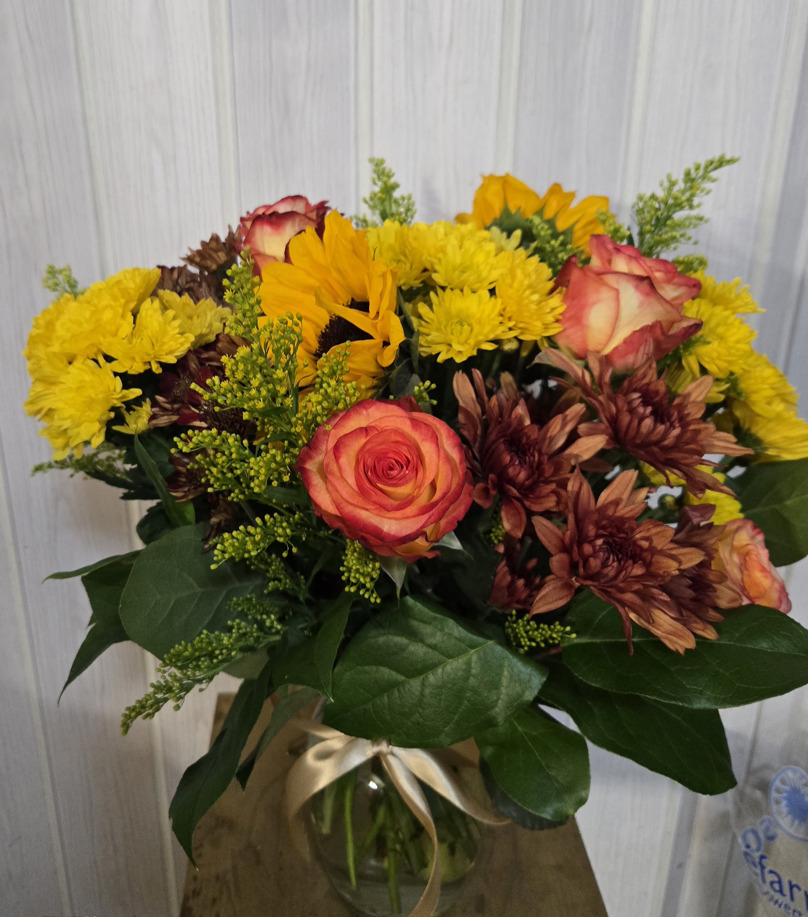 Autumn sunshine bouquet  - A radiant mix of golden yellow chrysanthemums, fiery orange roses, rustic bronze mums, and sunflowers — artfully arranged with lush greenery in a clear glass vase tied with a satin ribbon. Perfect for birthdays, Thanksgiving, or to brighten any day. 