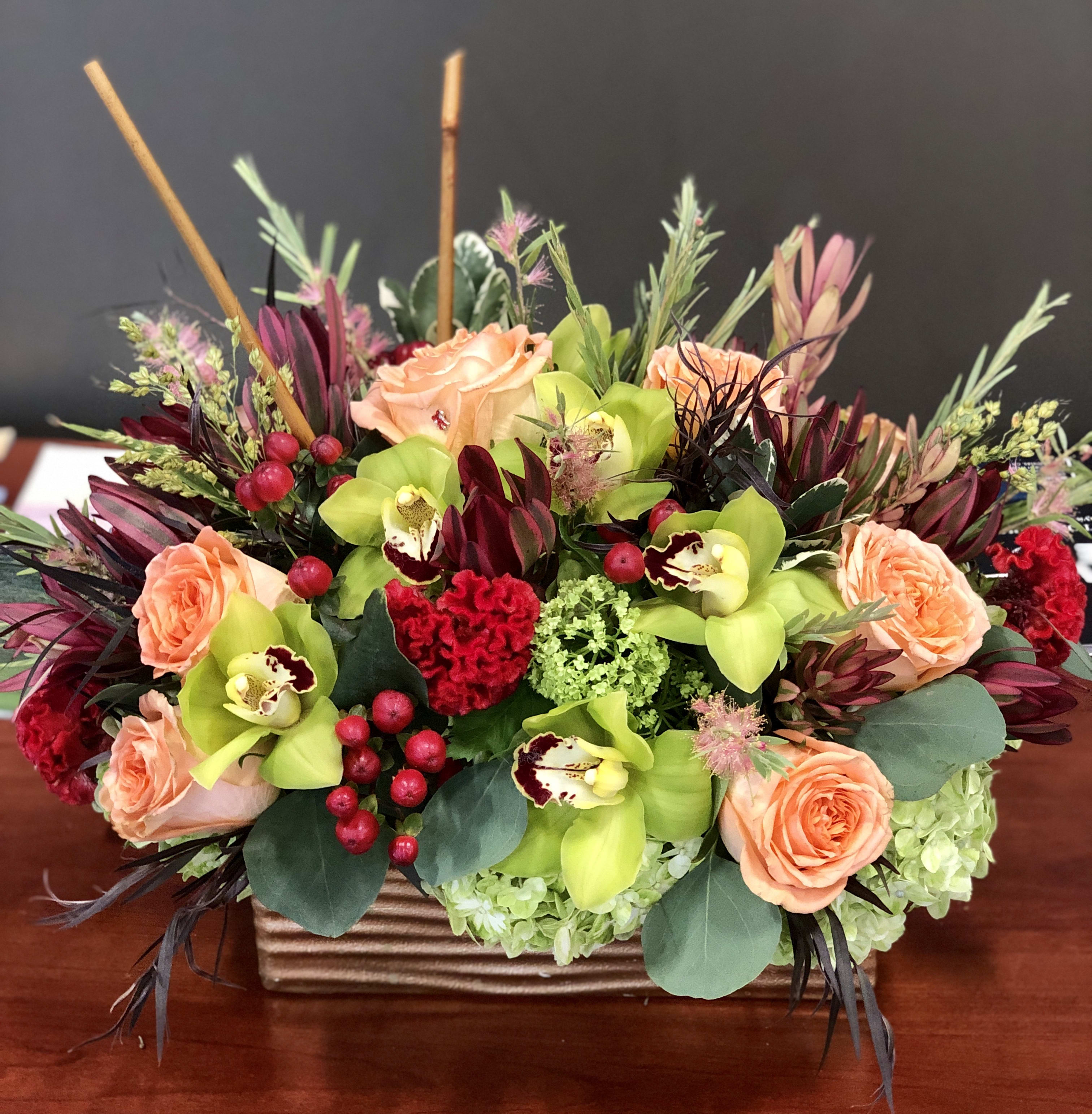 Peach roses and green orchids in a rectangular vase with red accents