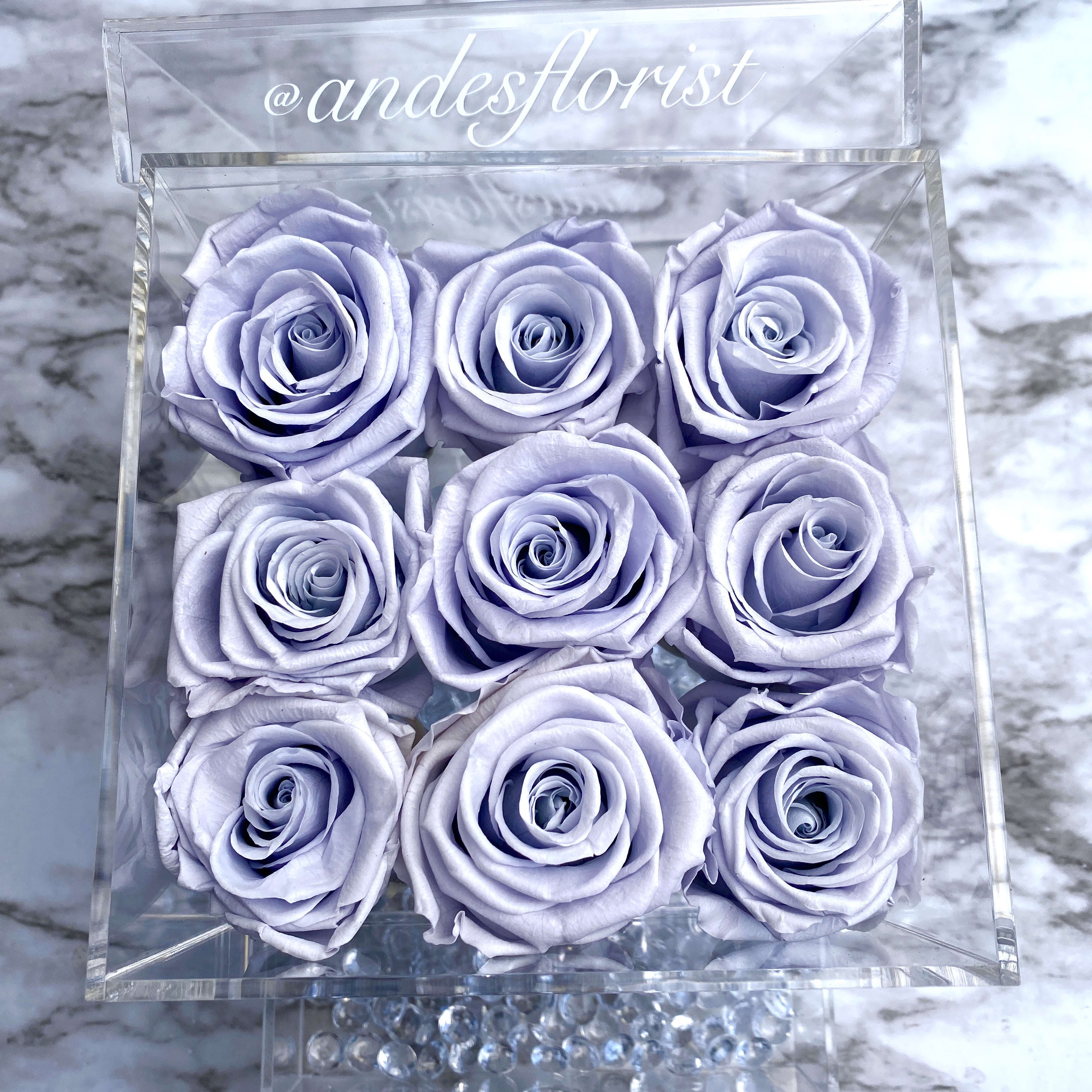 Nine lavender roses in a clear square box