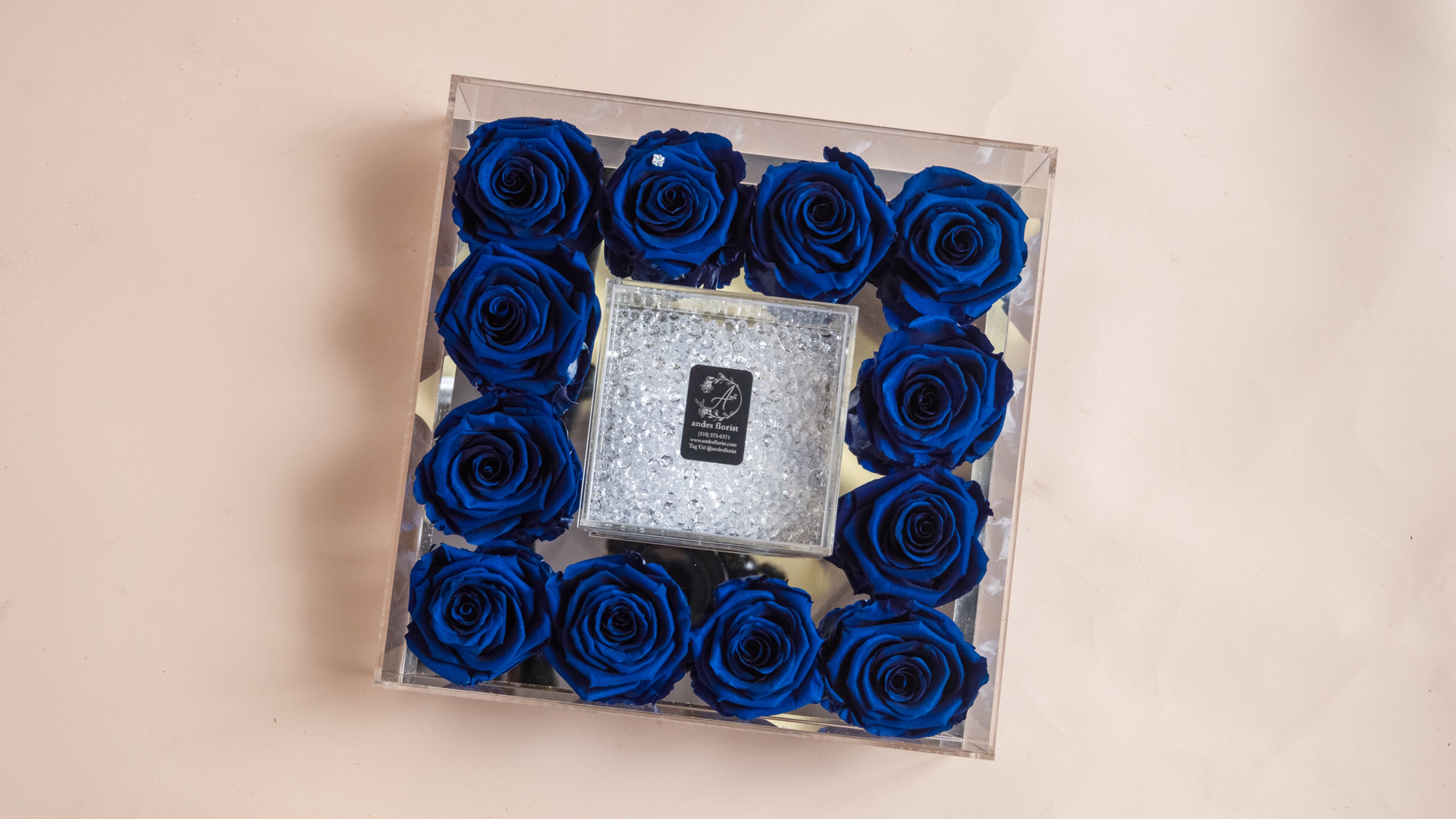Blue roses arranged in a clear square box with a glittery center