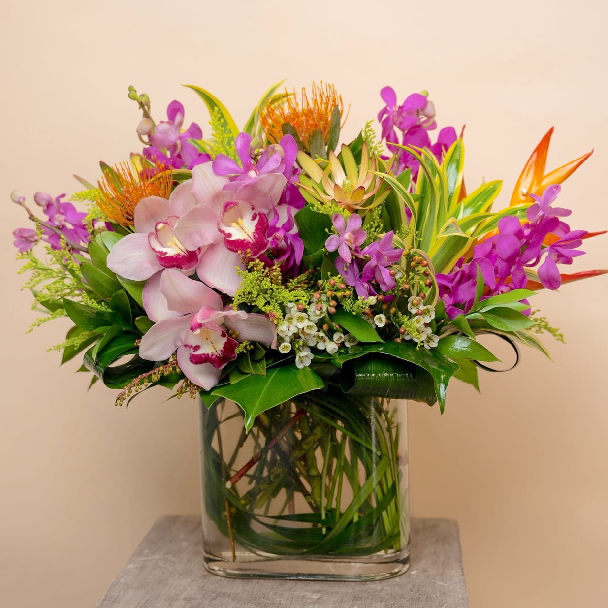 Tropical bouquet with orchids and orange pincushion blooms in a glass vase