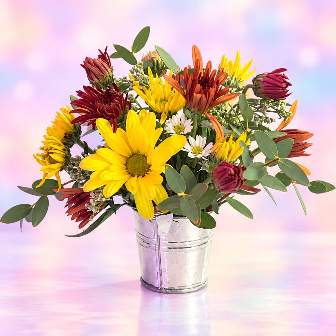 Mixed bouquet of yellow, burgundy, and orange daisies in a metal bucket