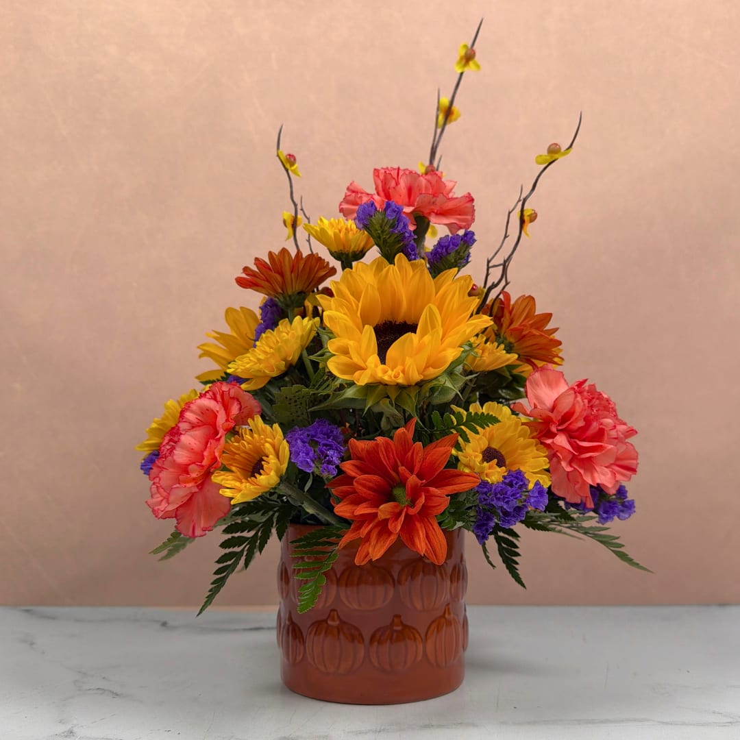 Colorful bouquet of sunflowers, carnations, and purple filler in an amber vase