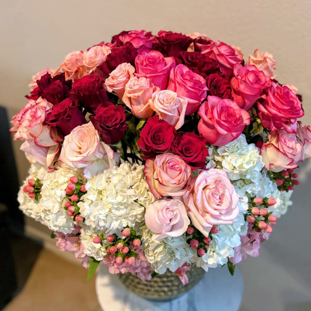 Round bouquet of pink, red, and white roses in a woven vase