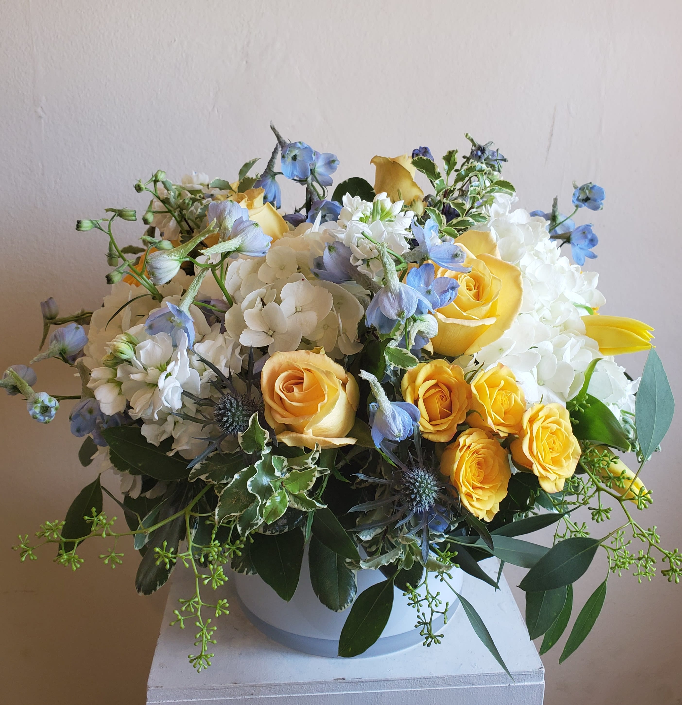 Bouquet of yellow roses, white hydrangeas, and blue flowers in a white vase