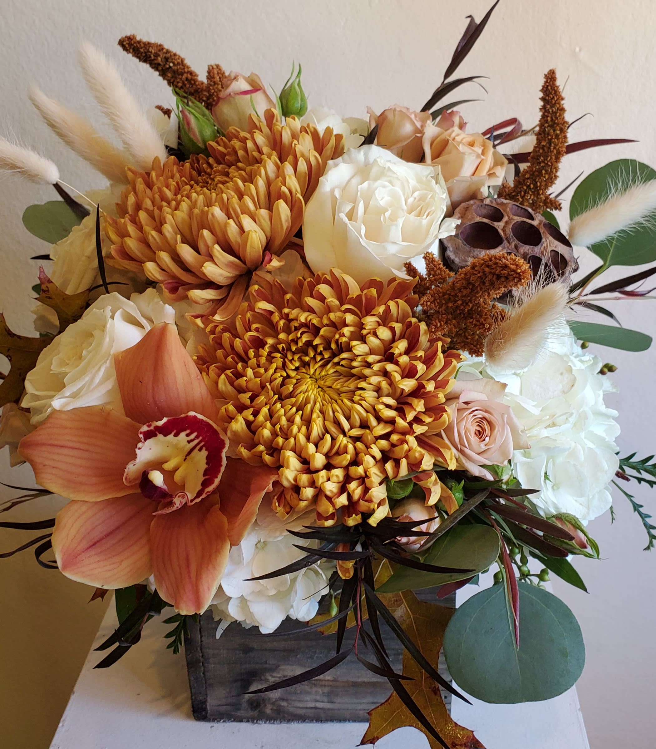 Autumn bouquet with orange chrysanthemums, white roses, and an orchid in a wooden box