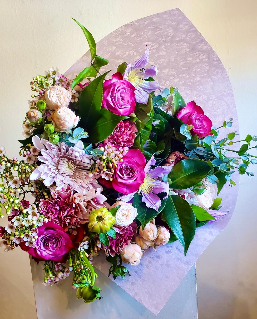 Bouquet of pink roses, lavender flowers, and mixed blooms wrapped in pale paper