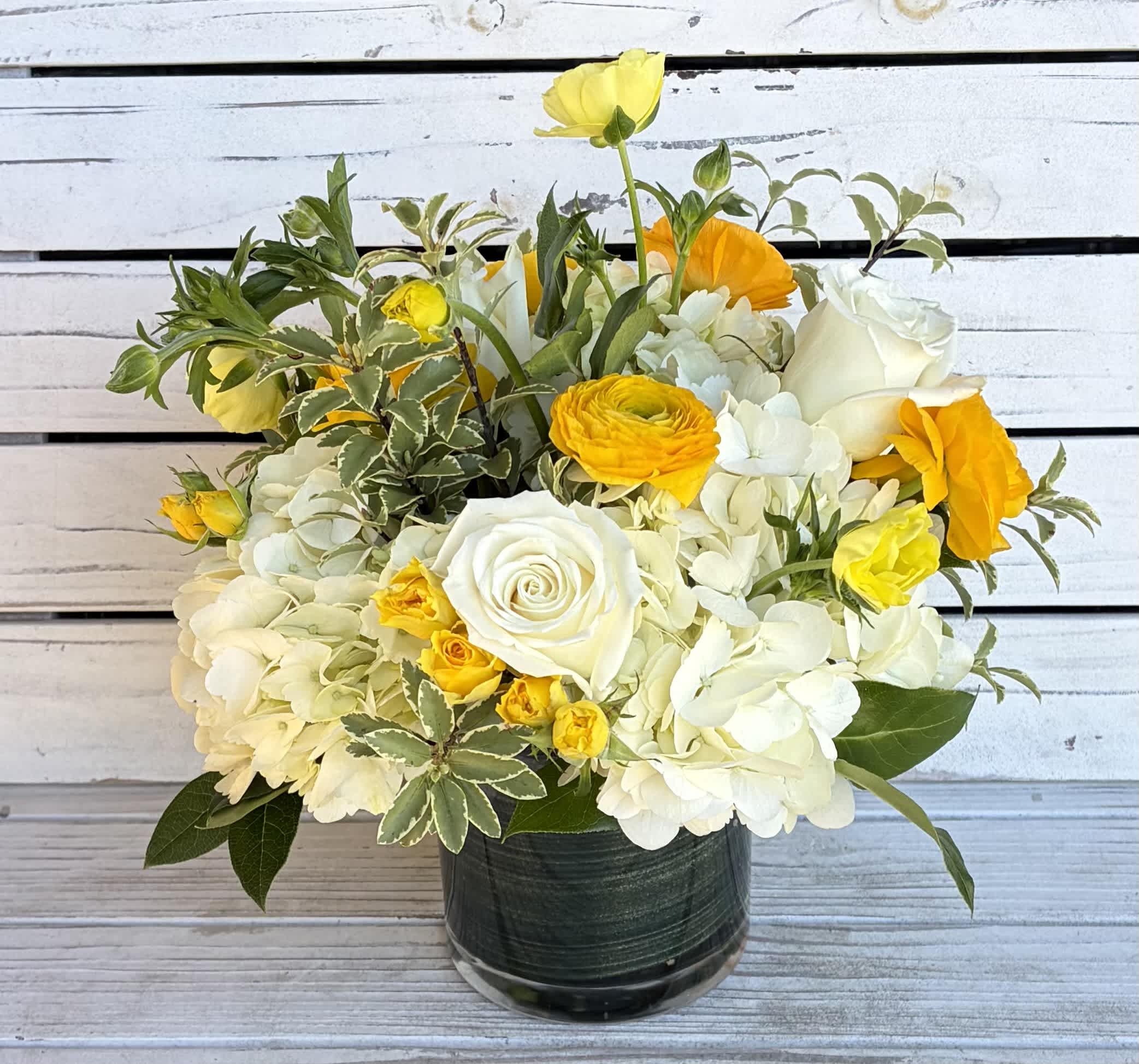 White and yellow flower arrangement in a dark glass vase