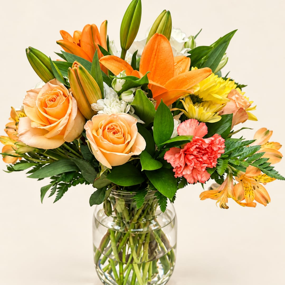 Orange lilies, peach roses, and yellow flowers in a clear glass vase