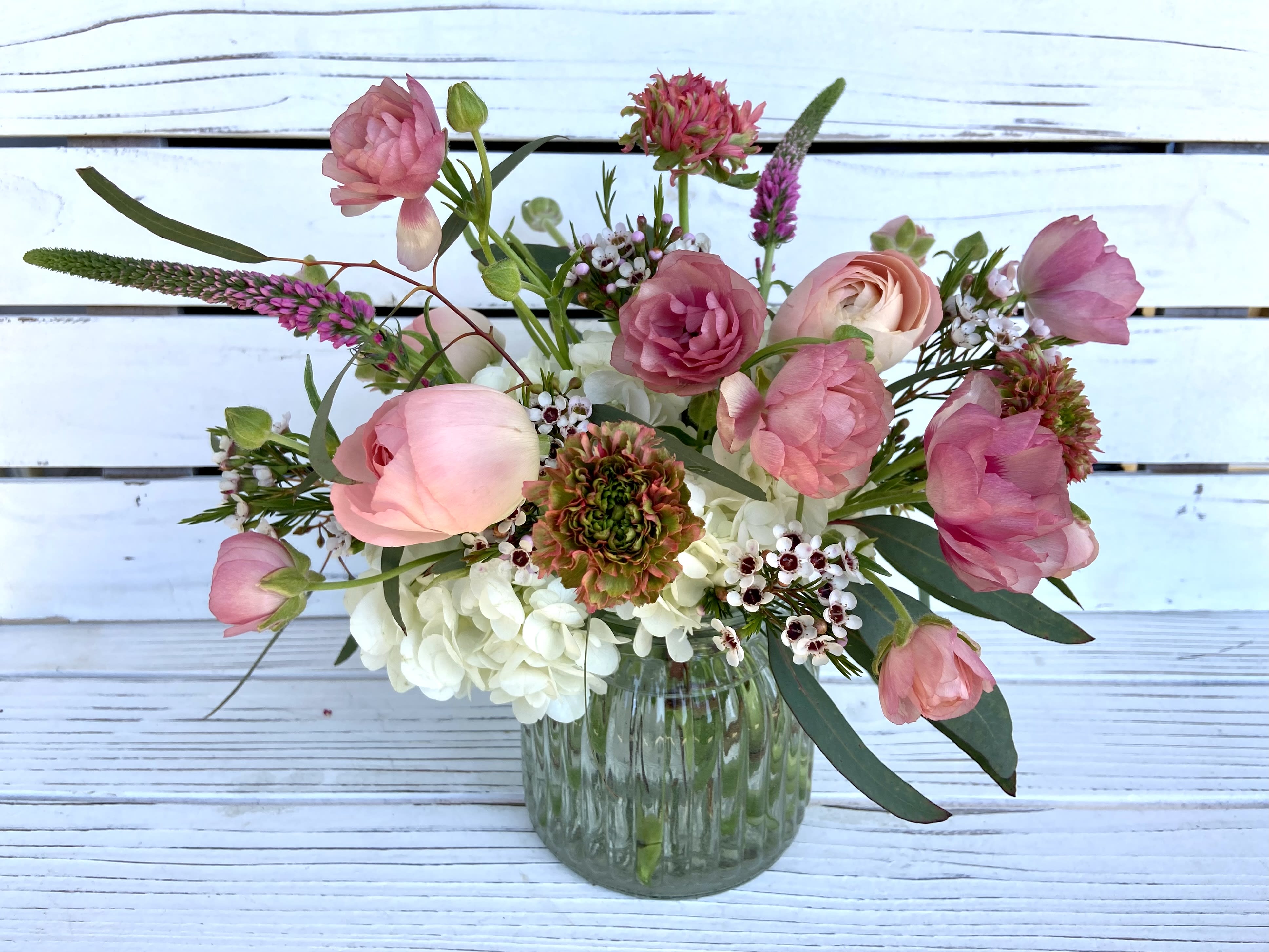 Small glass vase with pink ranunculus and mixed flowers in a loose, airy arrangement