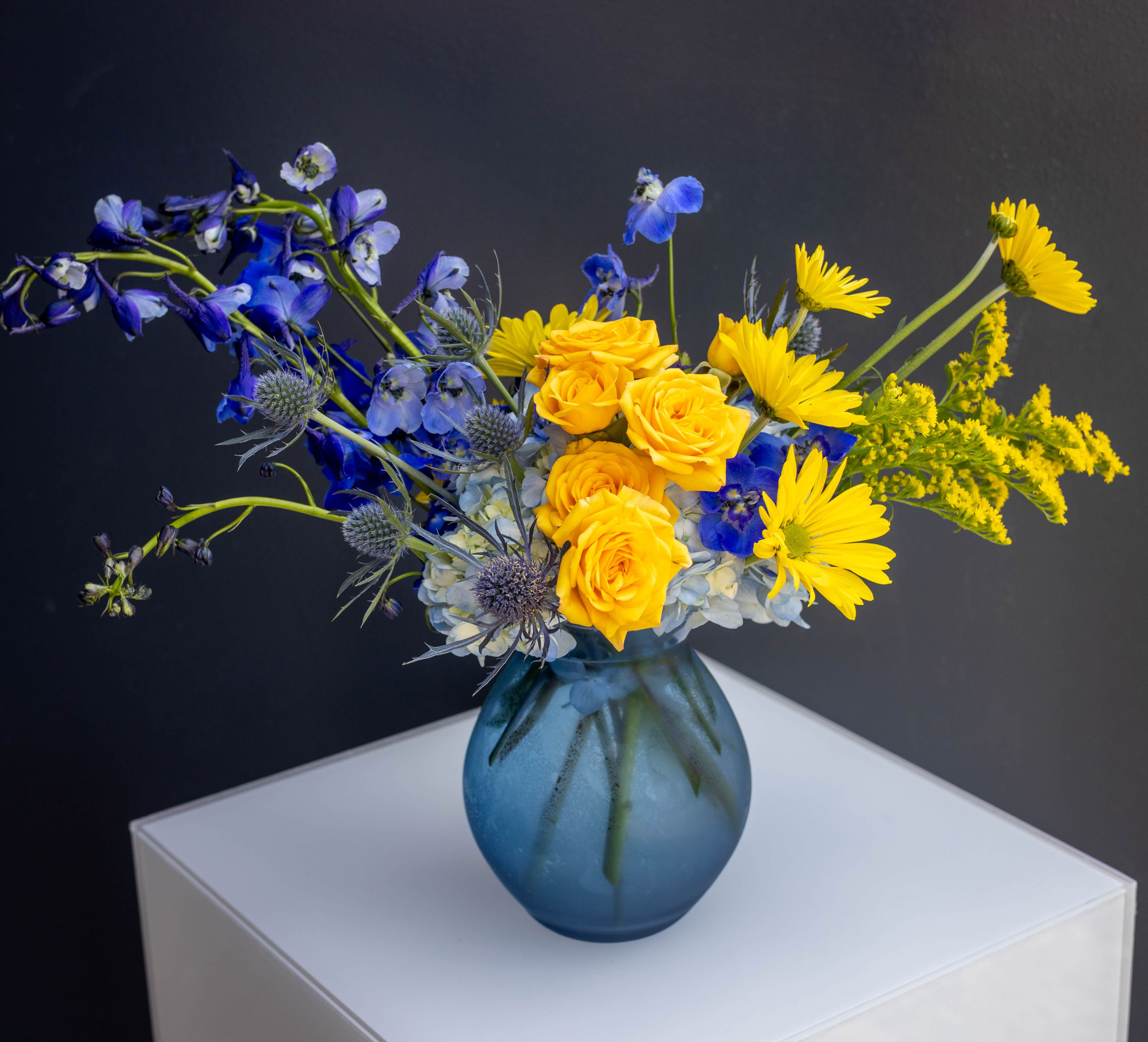 Blue and yellow flower arrangement in a blue glass vase