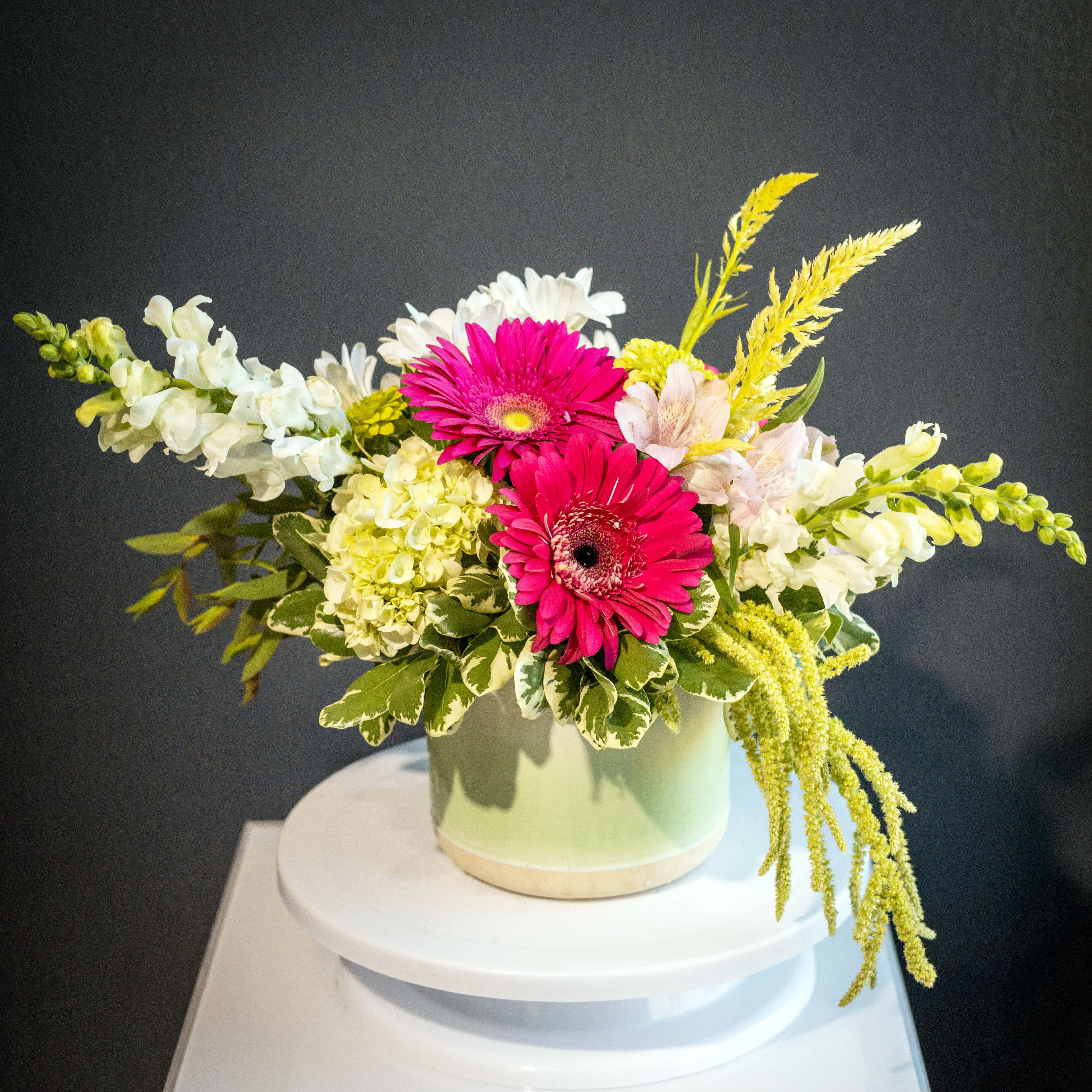 Pink gerbera daisies and white flowers arranged in a pale green vase