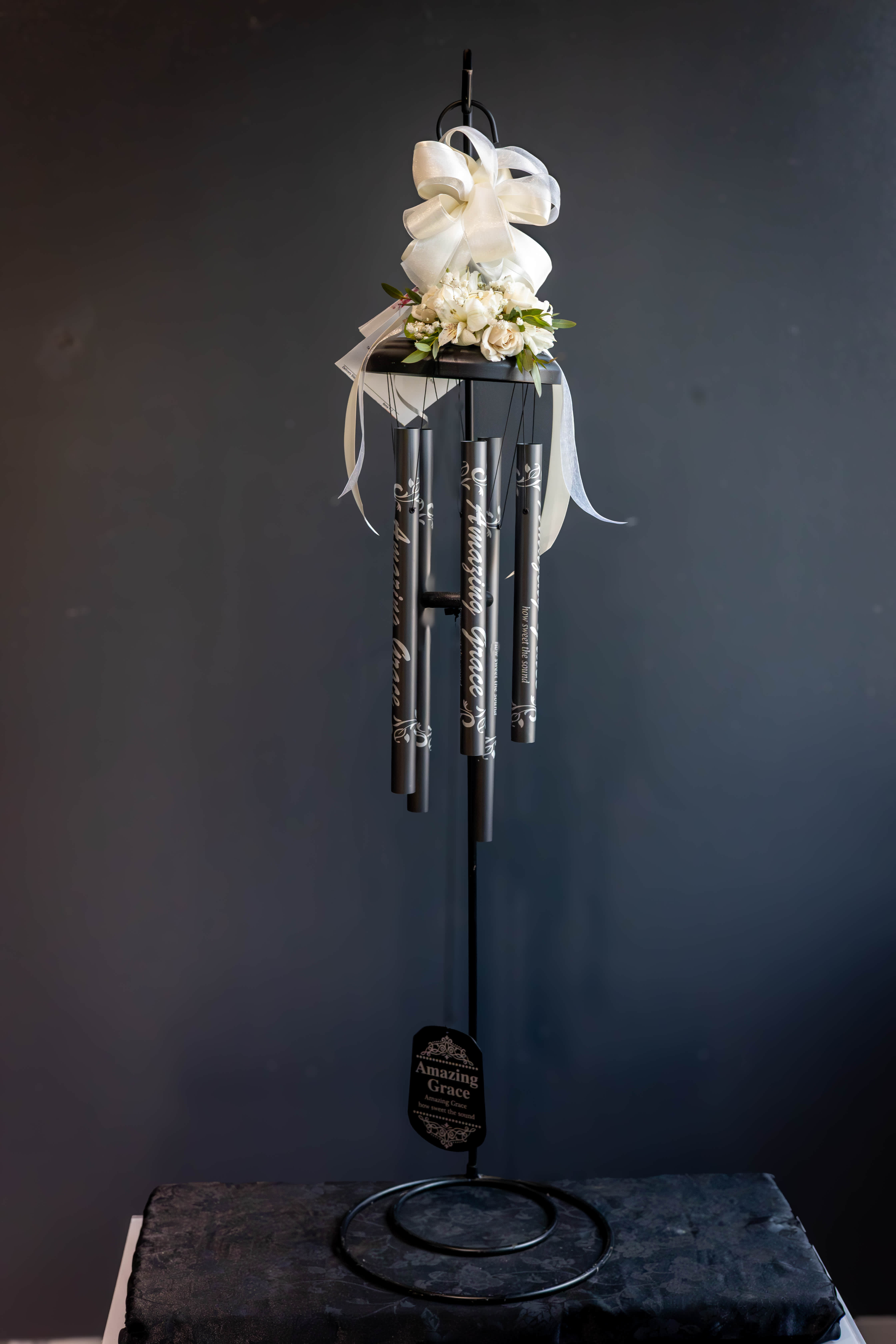 White floral topper with ribbon on a black wind chime stand