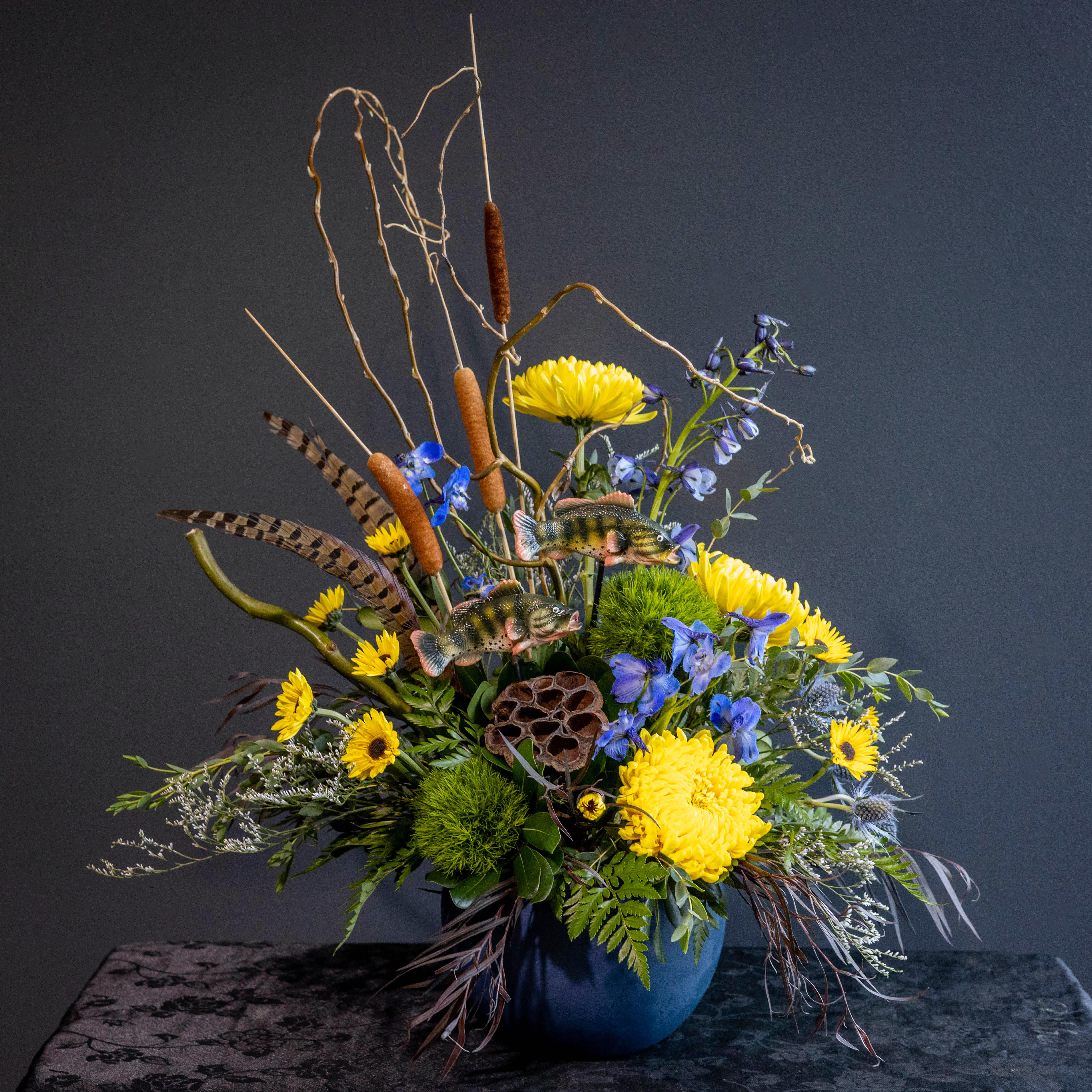 Tall floral arrangement with yellow chrysanthemums and blue flowers in a blue vase
