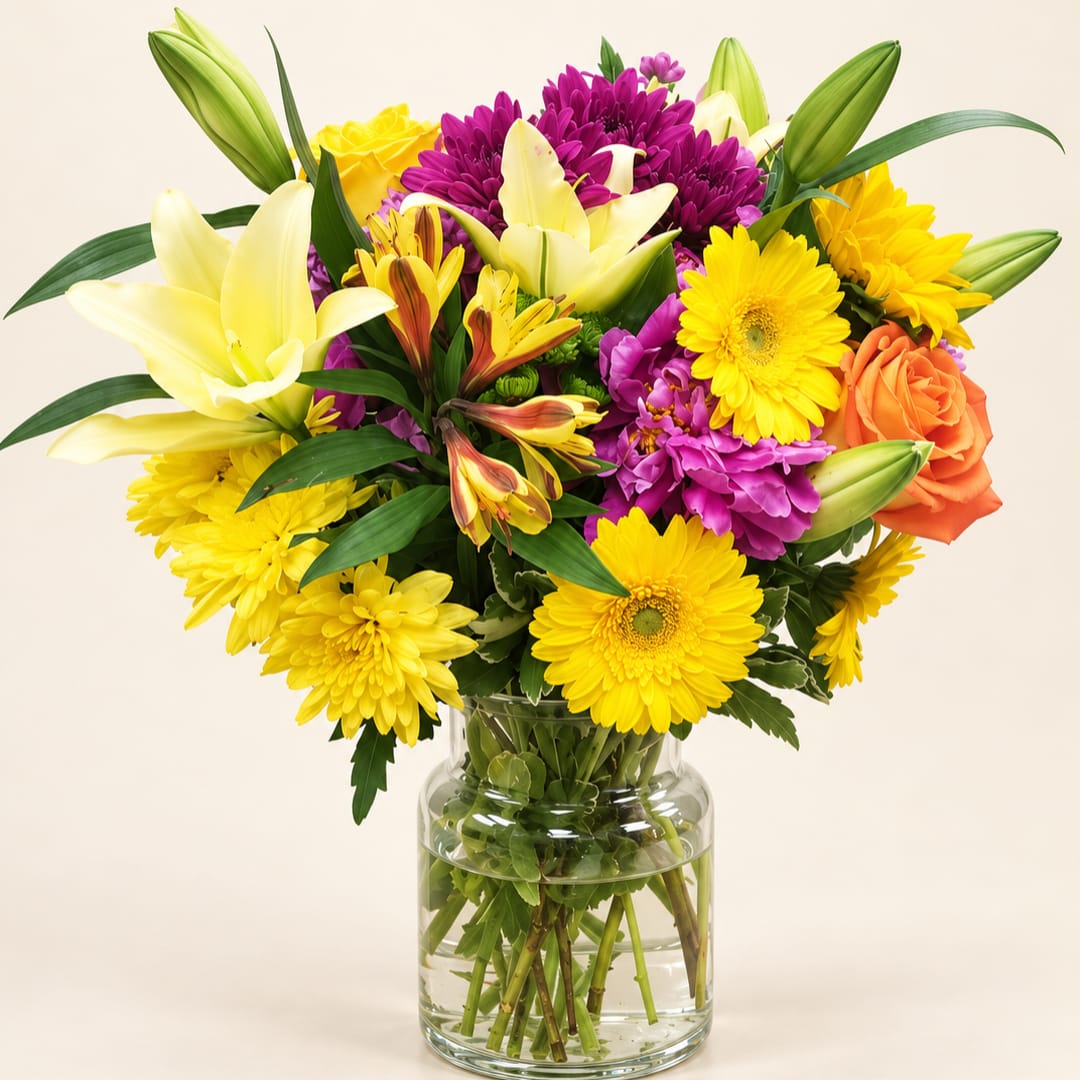Colorful mixed bouquet in a clear glass vase with lilies, daisies, and roses